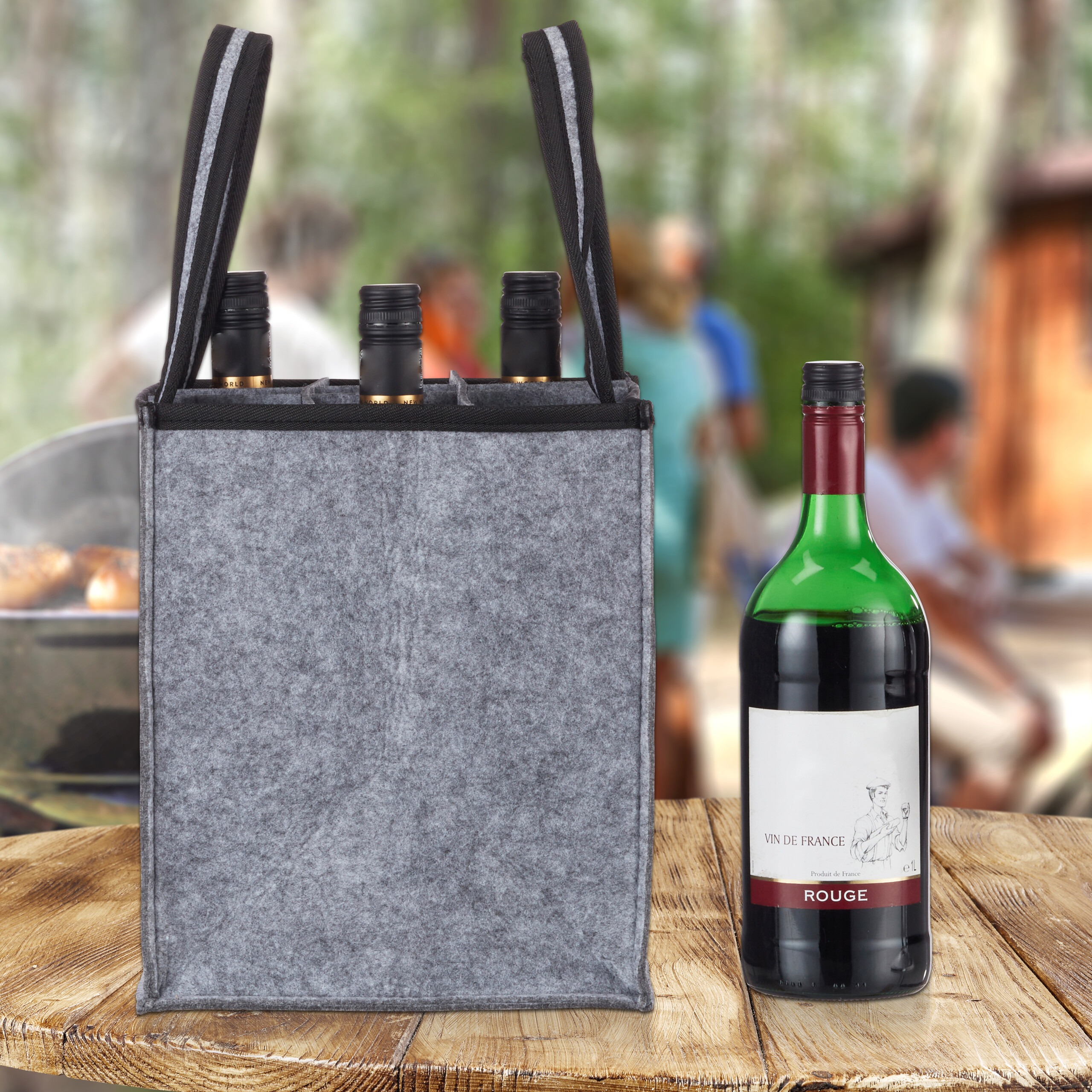Eine graue Filz-Weintasche mit drei Flaschen steht auf einem Holztisch, eine Flasche daneben, verschwommener Hintergrund.