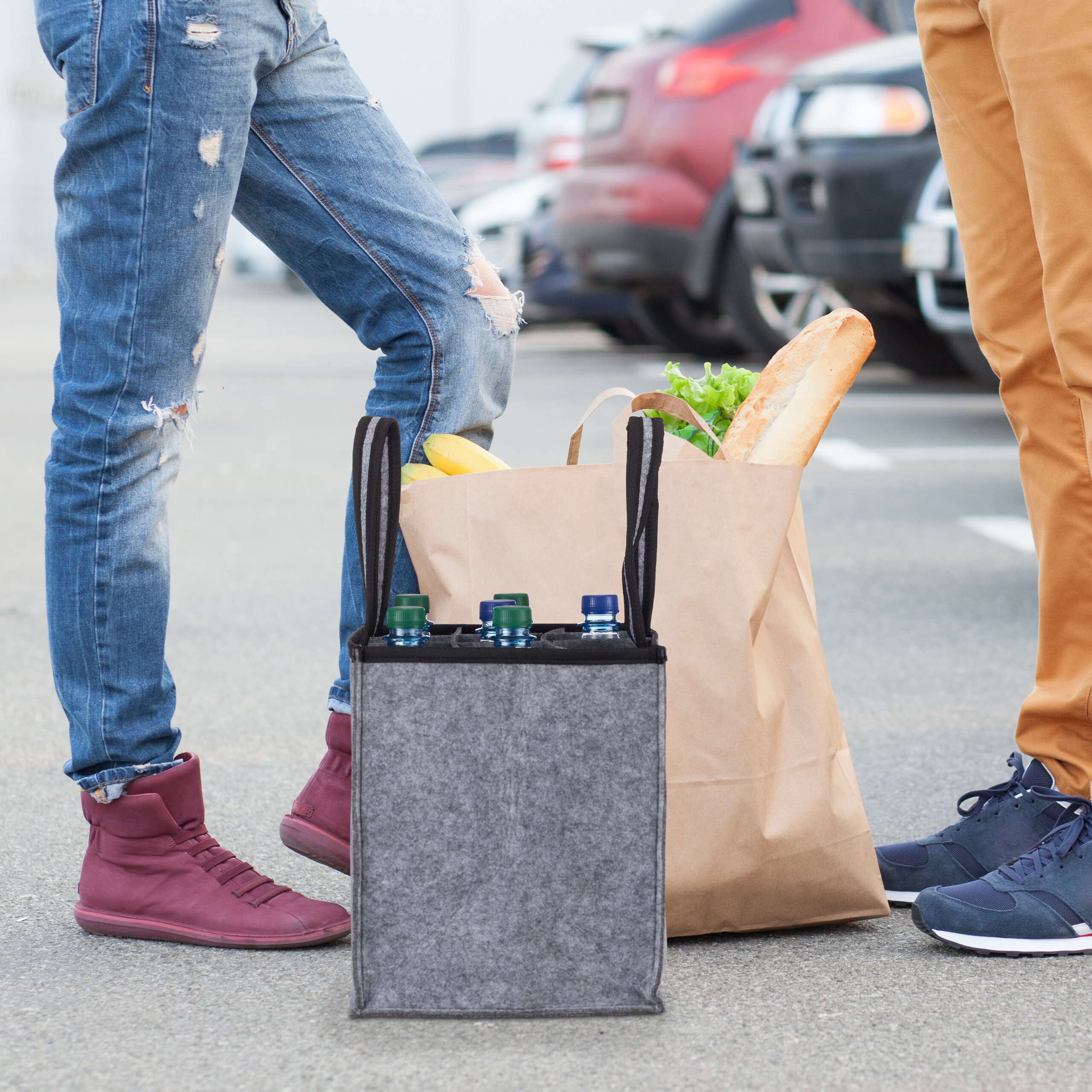 Zwei Personen stehen mit einer Filzflaschentasche und einer Papiertüte voller Brot und Gemüse auf einem Parkplatz.