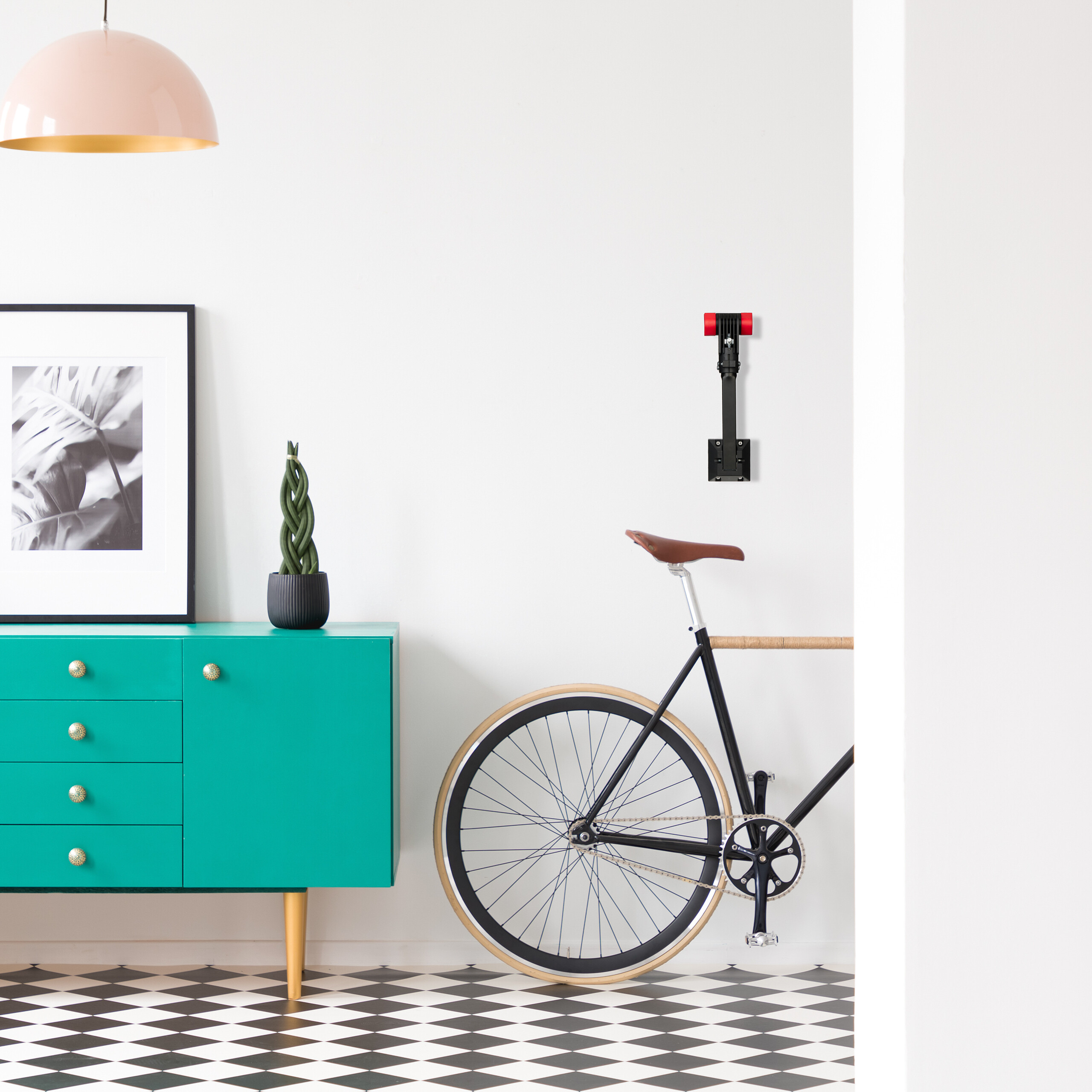 Ein raum mit schwarz-weißem Fliesenboden, einer grünen Kommode, einem Fahrrad an der Wand und einem rosafarbenen Hängelampenschirm.