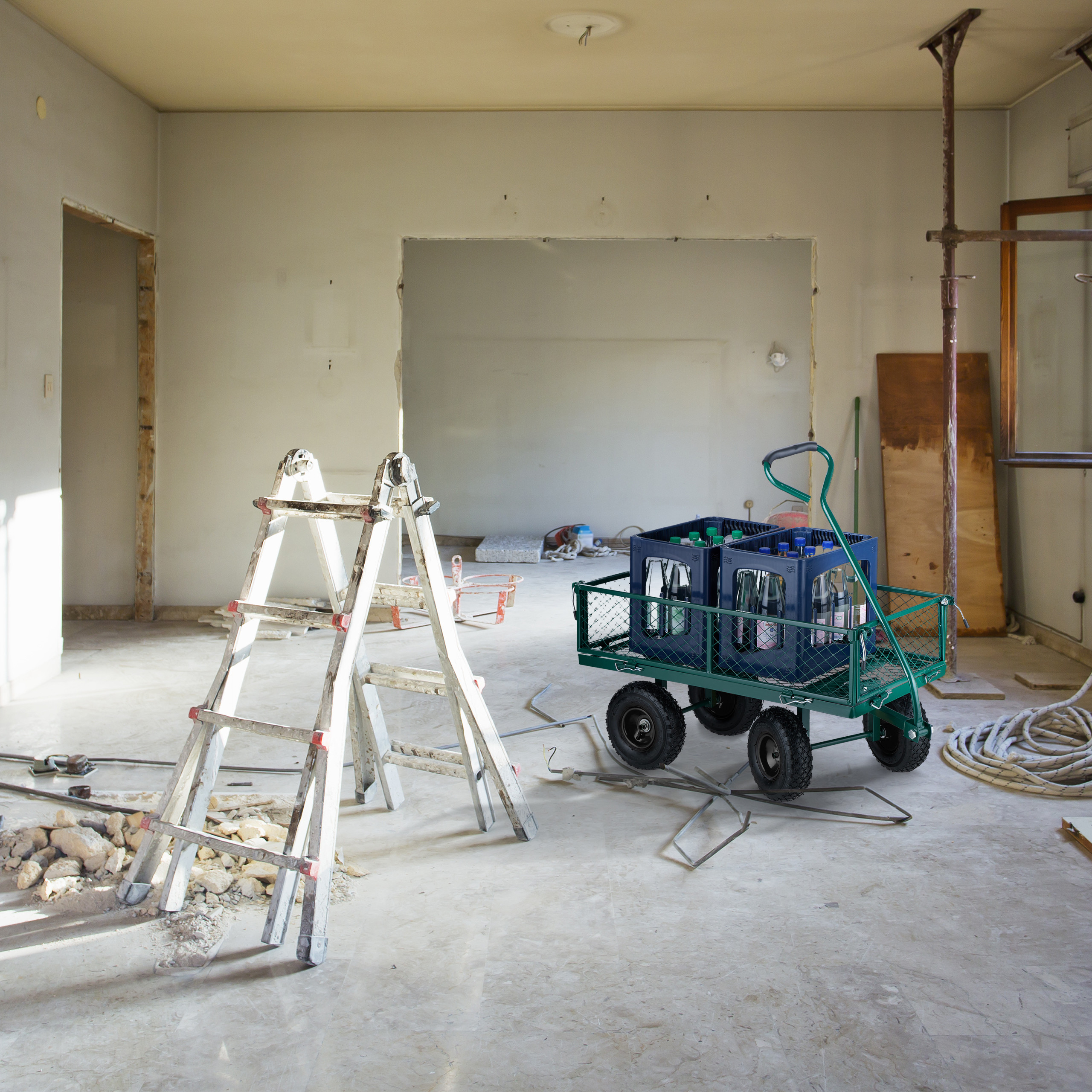 Ein renovierungsbedürftiger Raum mit einer Leiter, Trümmern und einem grünen Transportwagen mit Kisten.