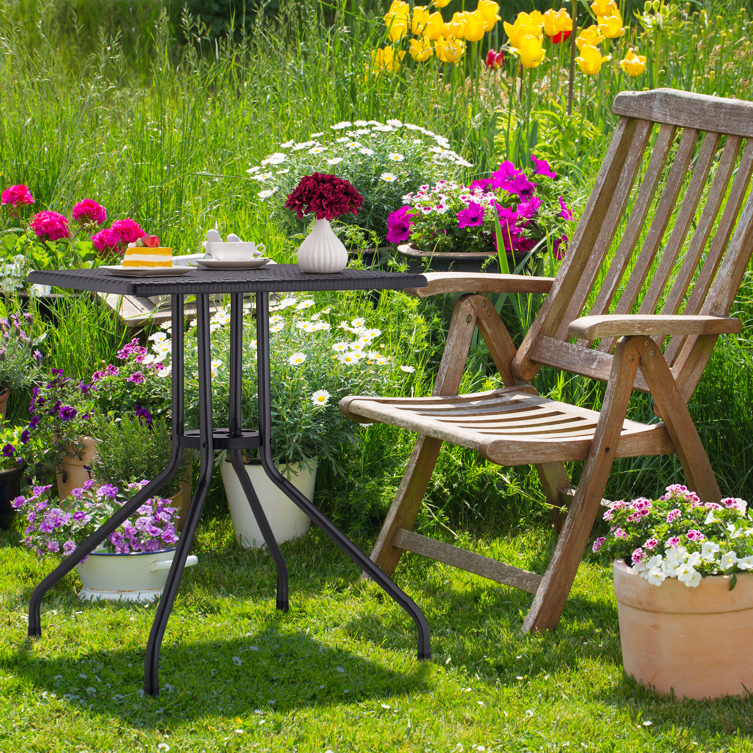Ein Holzsessel und ein schwarzer Tisch mit Kuchen und Blumen stehen in einem üppigen Garten.
