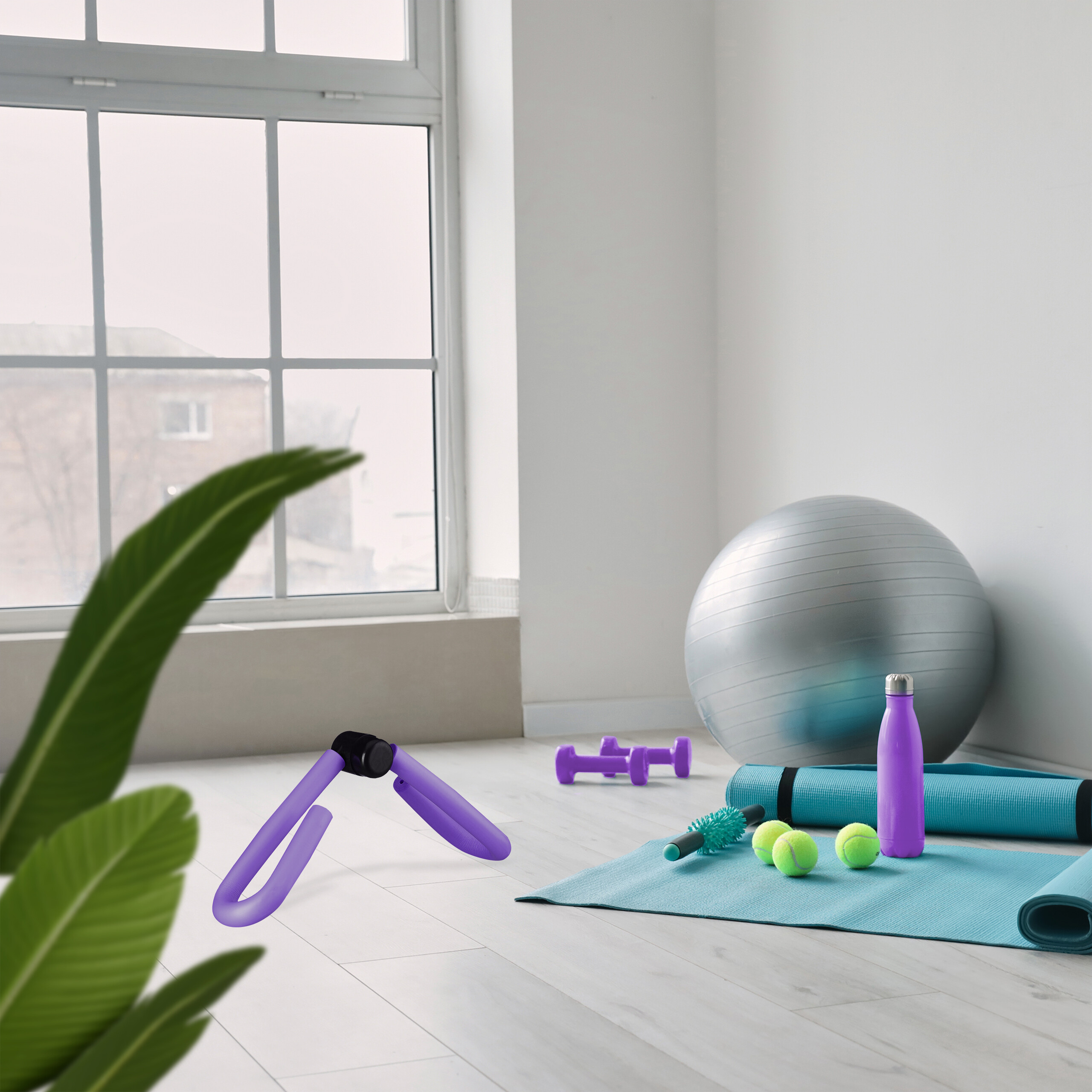 Fitnessgeräte auf dem Boden: Yogamatte, Übungsball, Hanteln und Flasche vor einem großen Fenster.
