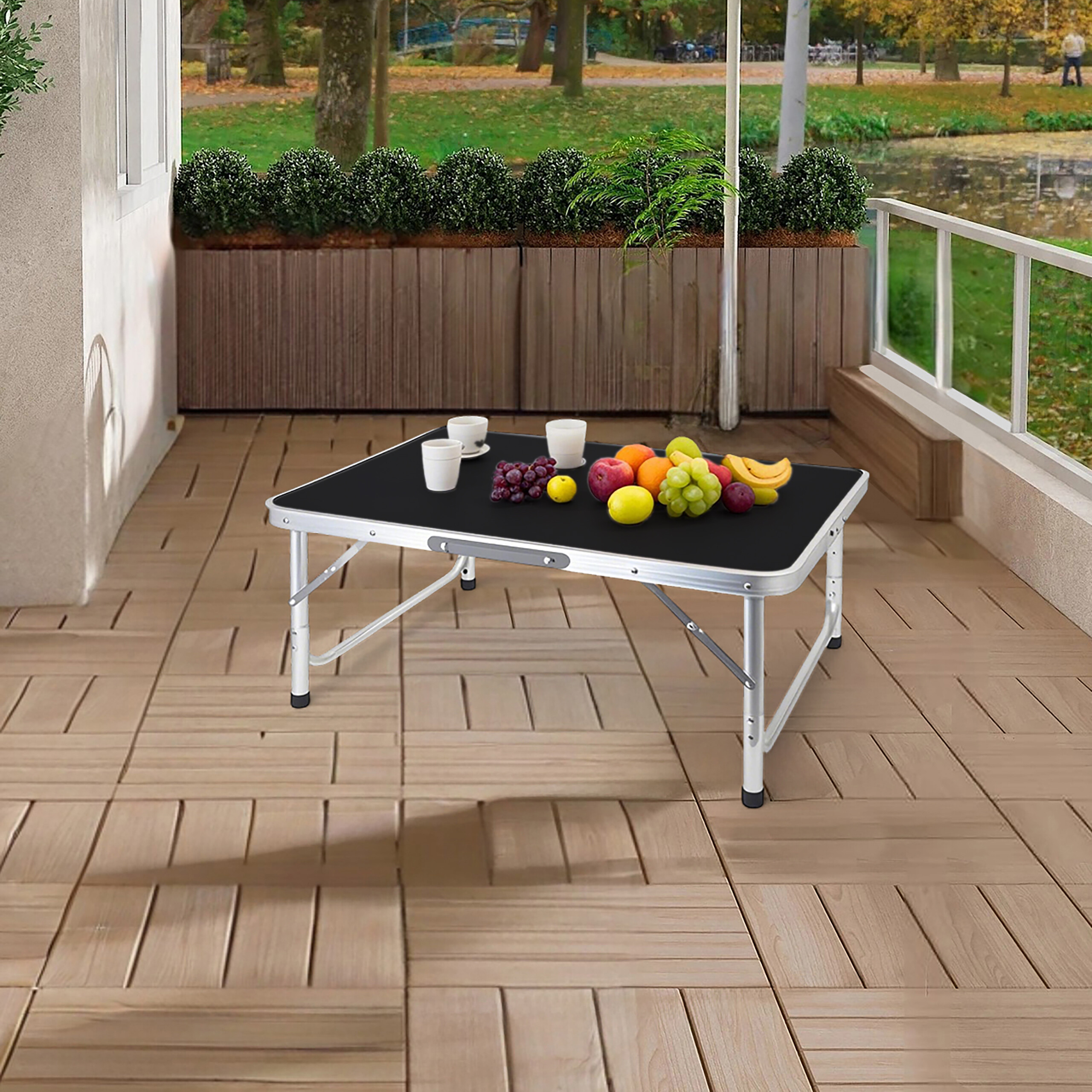 Ein tragbarer Tisch mit Früchten und Tassen steht auf einer gefliesten Terrasse im Freien.
