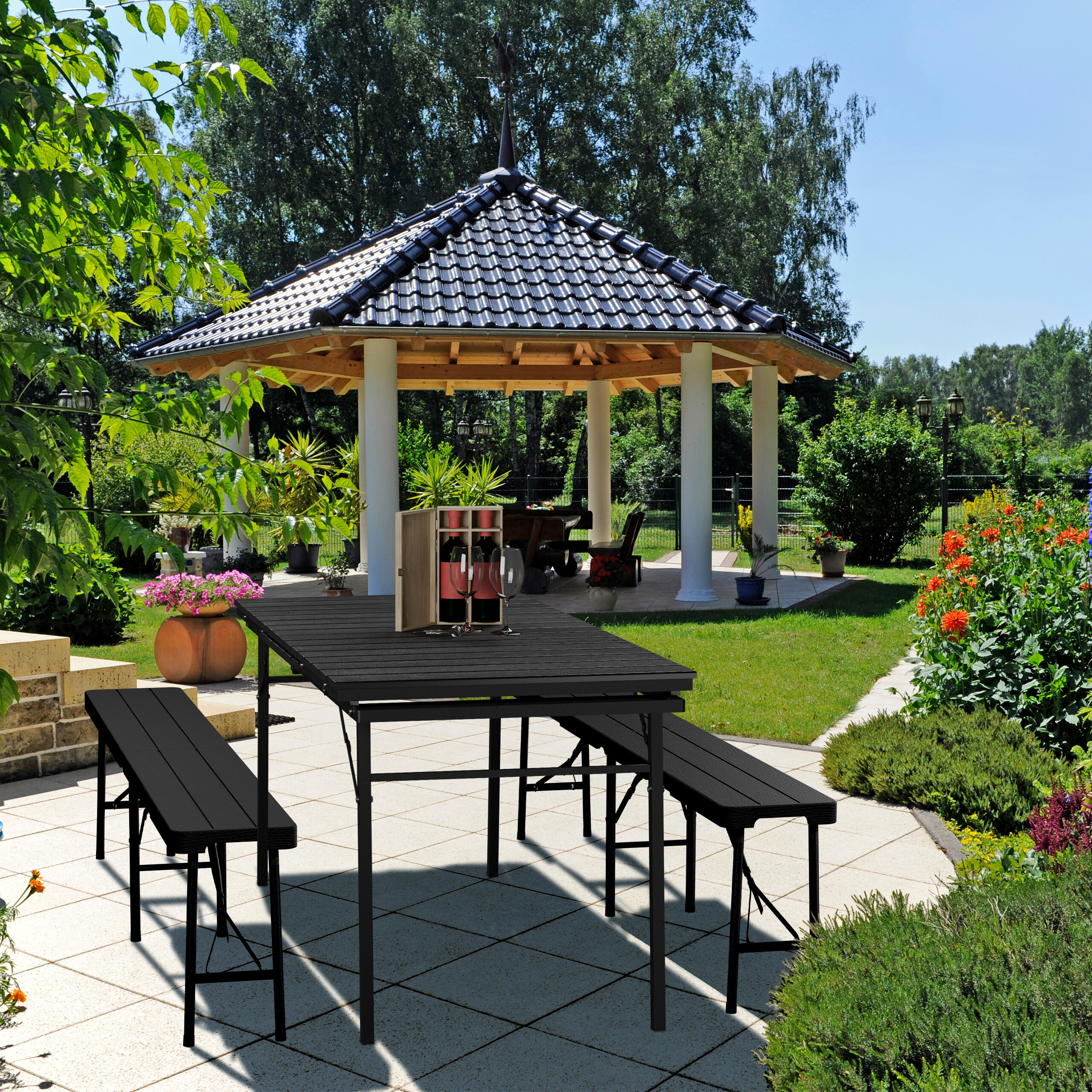 Ein schwarzer Holztisch mit Bänken auf einer Terrasse, im Hintergrund ein Pavillon und ein Garten.