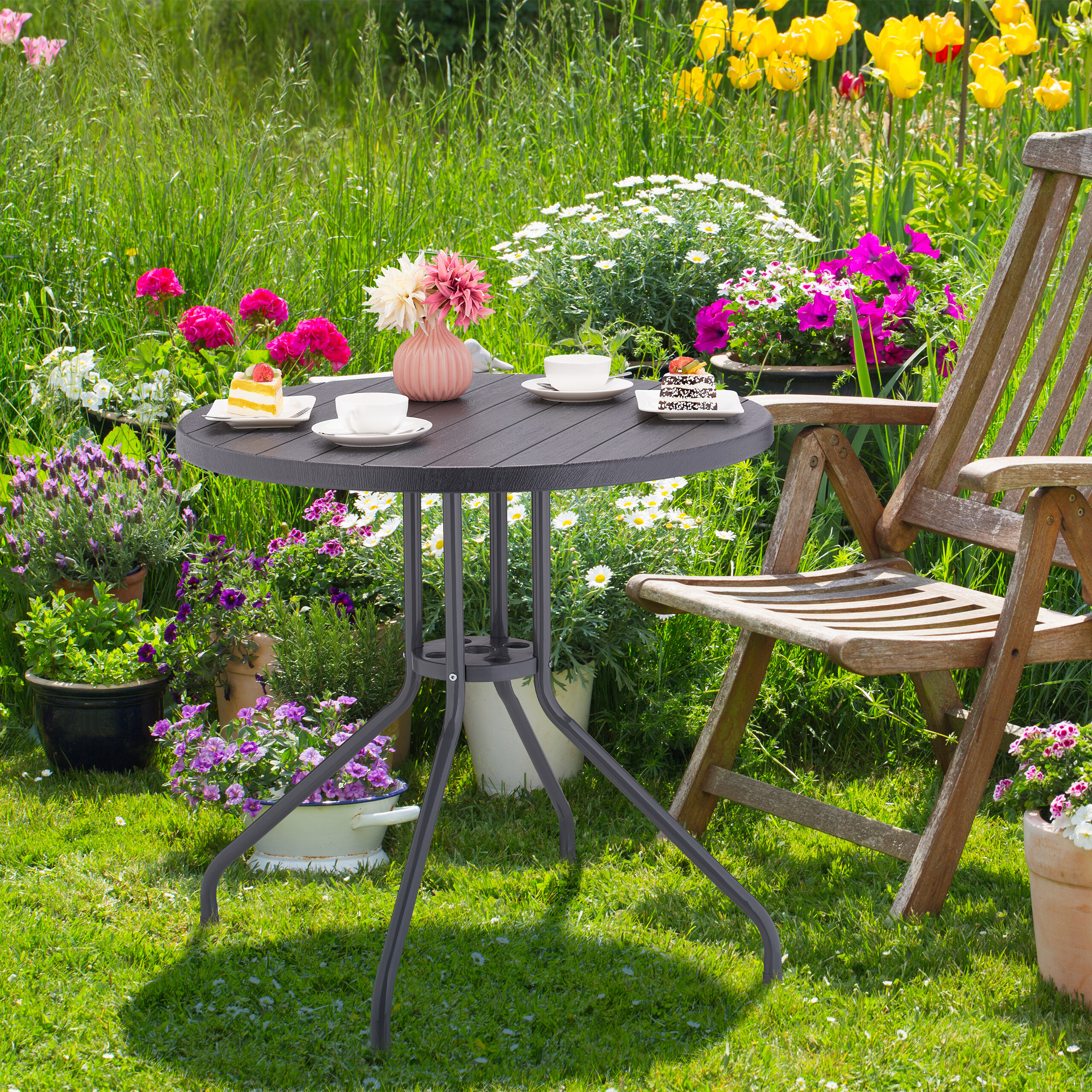 Ein runder Tisch mit Tassen, Kuchen und einer Vase in einem üppigen Garten mit bunten Blumen.