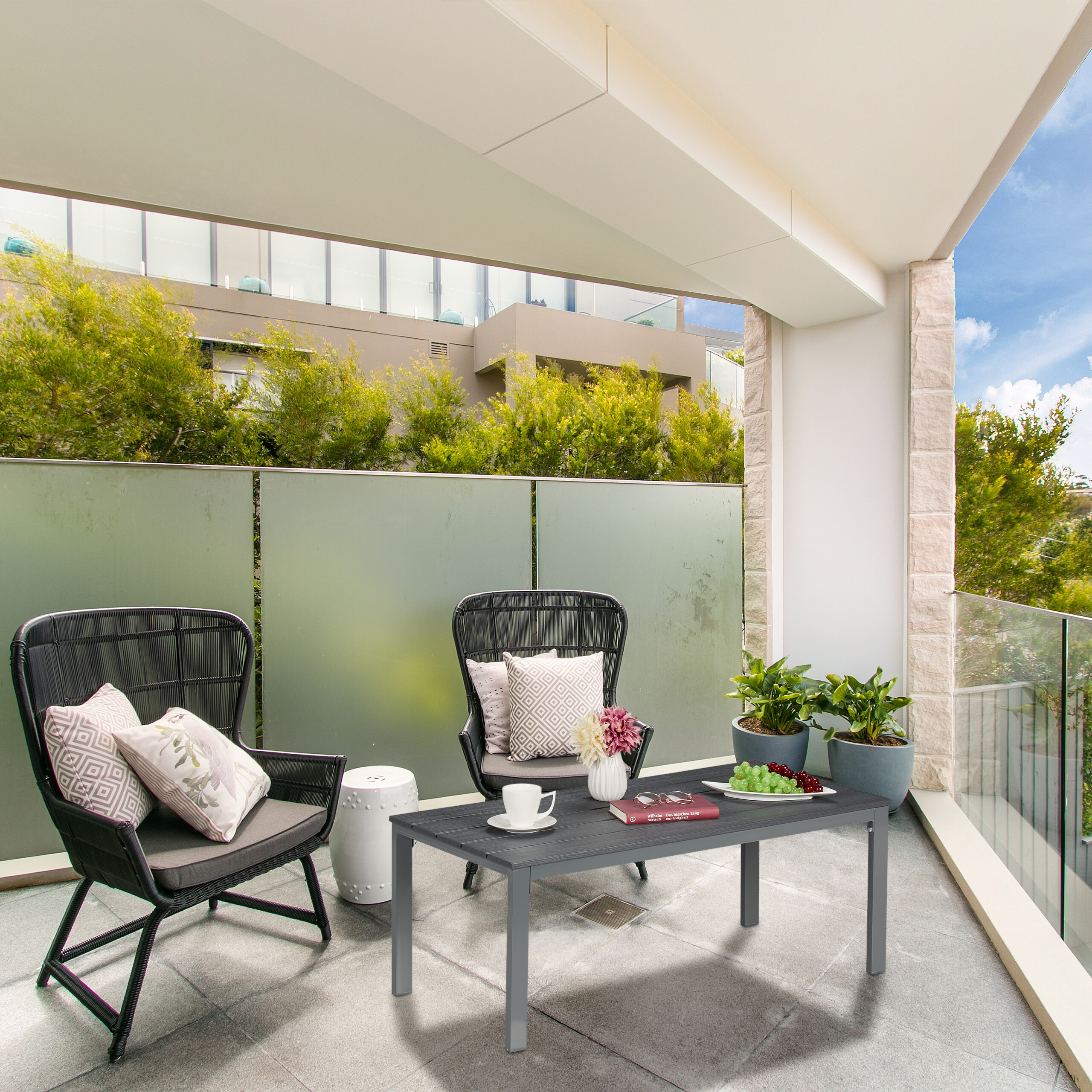 Ein moderner Balkon mit zwei schwarzen Korbsesseln, einem Kaffeetisch und Topfpflanzen an einer Glasbrüstung.