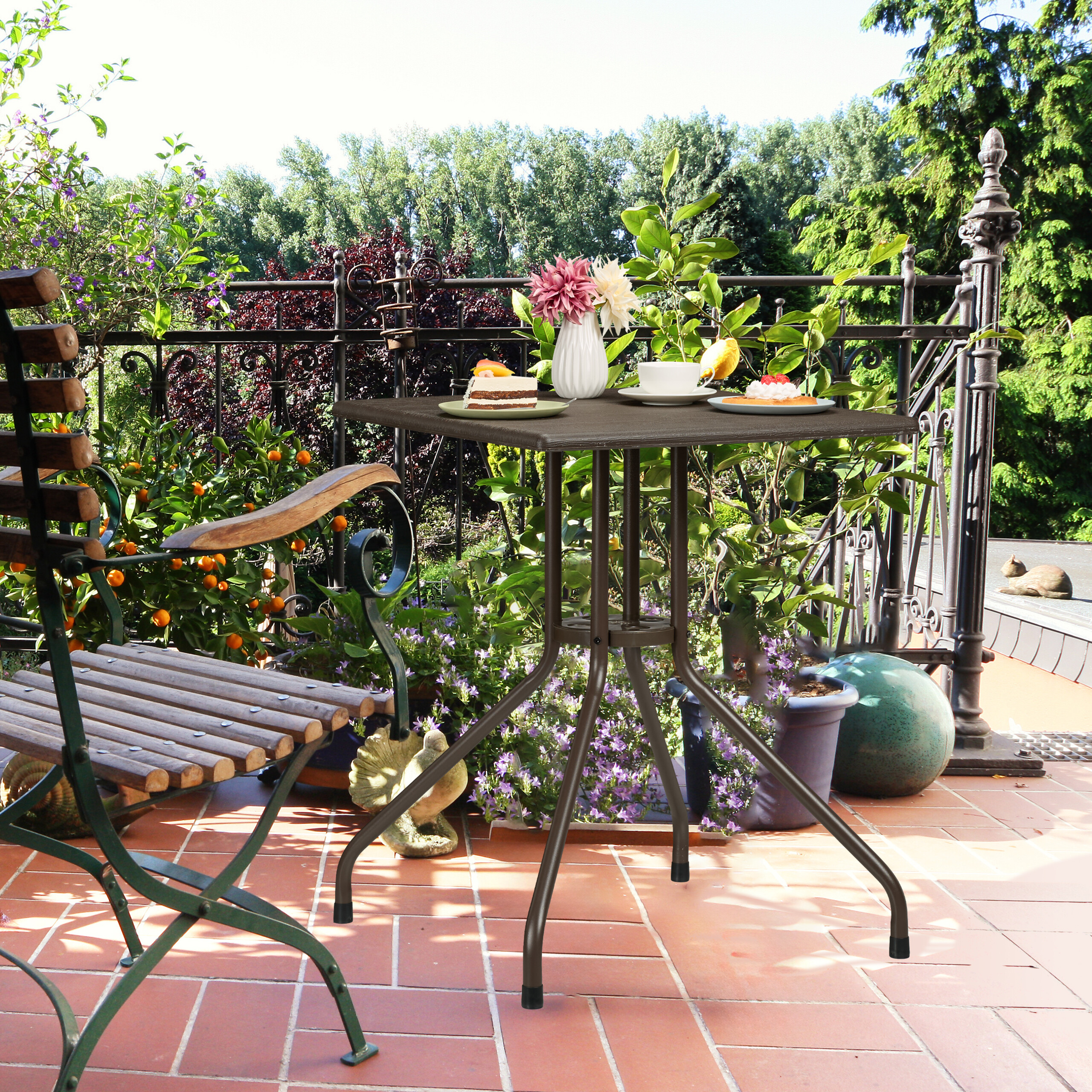 Ein Kaffeetisch mit Torte und Blumen auf einer sonnigen Terrasse, umgeben von Grünpflanzen.