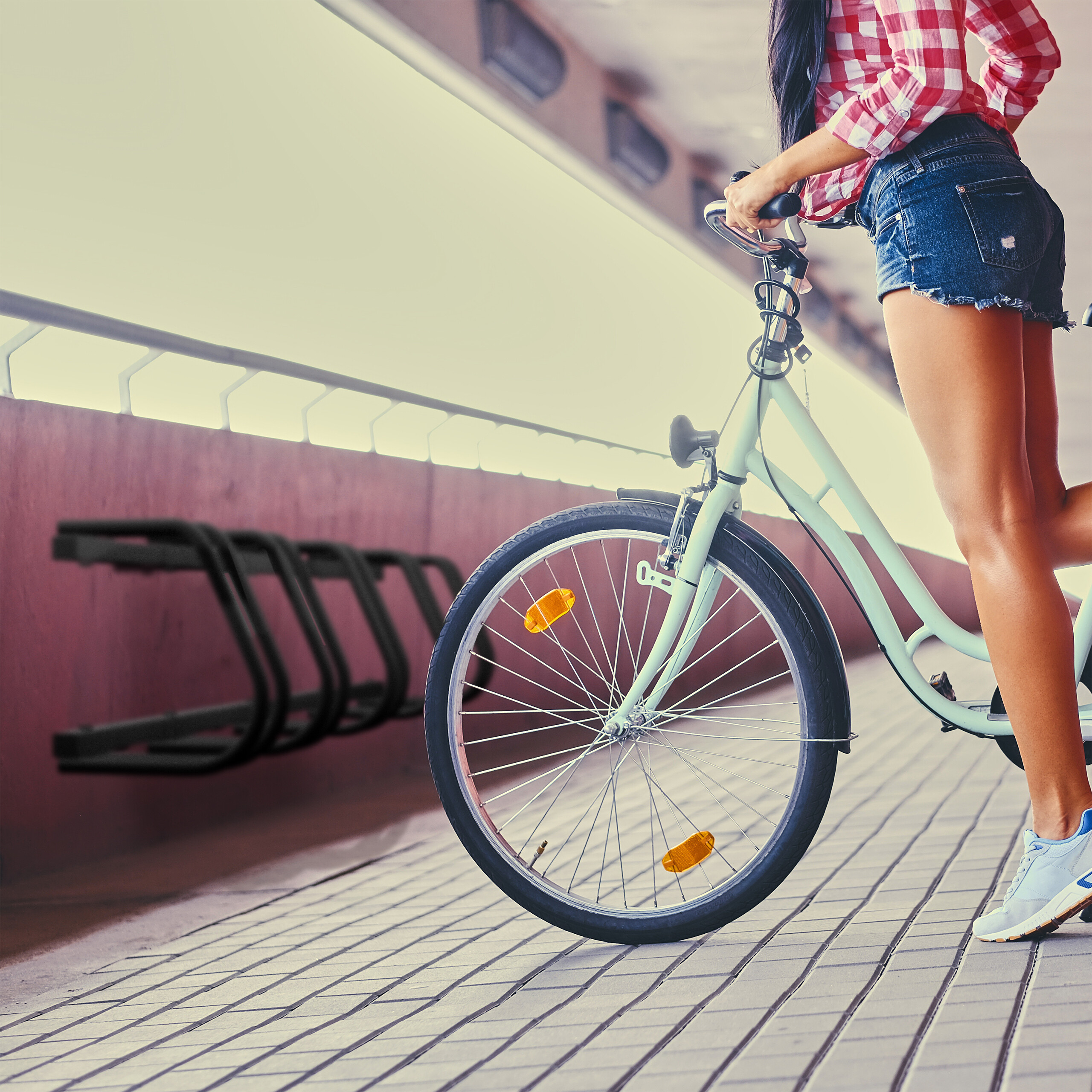 Eine Frau in roten Karohemd und Jeansshorts steht mit einem hellblauen Fahrrad auf einer gepflasterten Brücke.