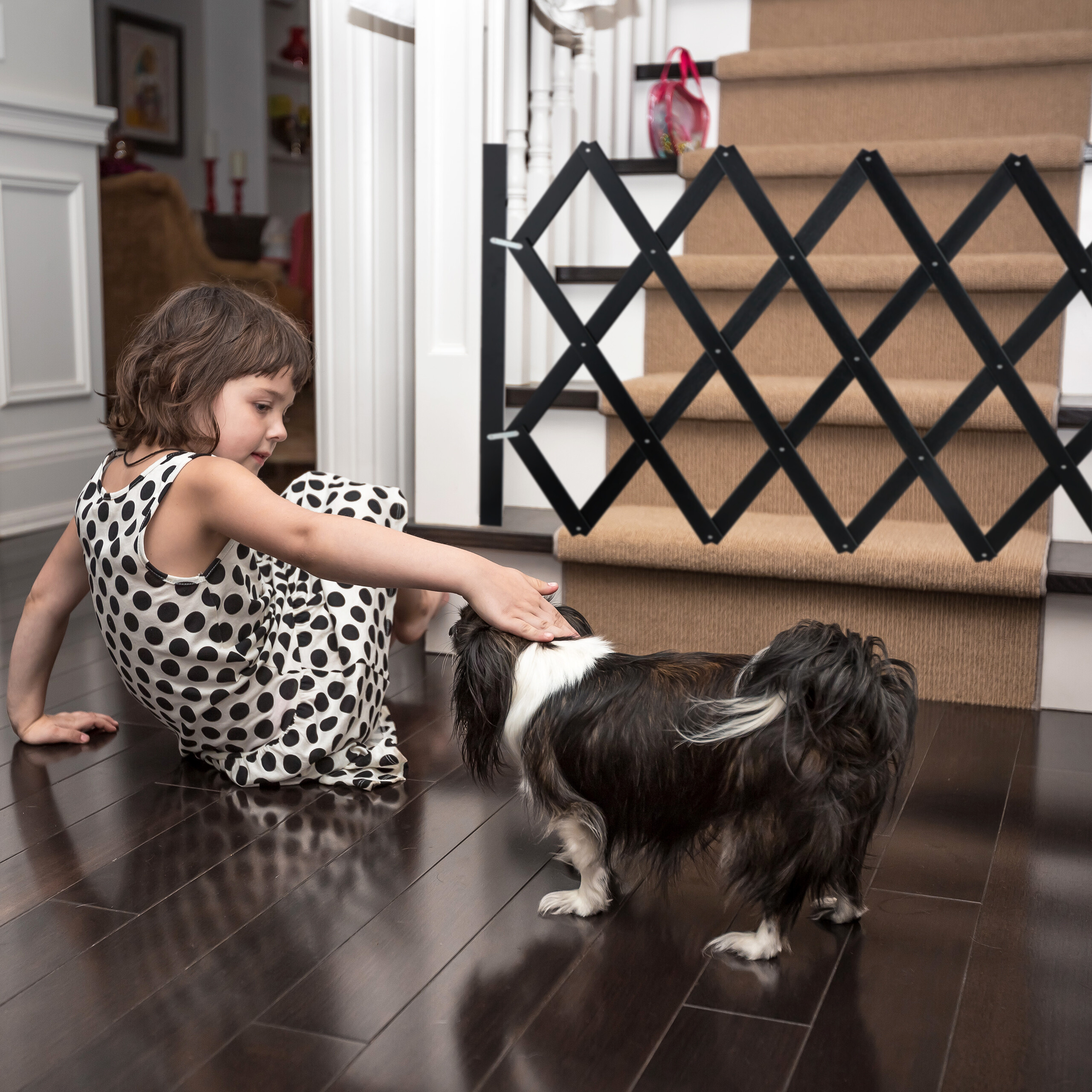 Ein junges Mädchen in einem schwarz-weißen Polokleid streichelt einen kleinen schwarz-weißen Hund vor einer Treppe.