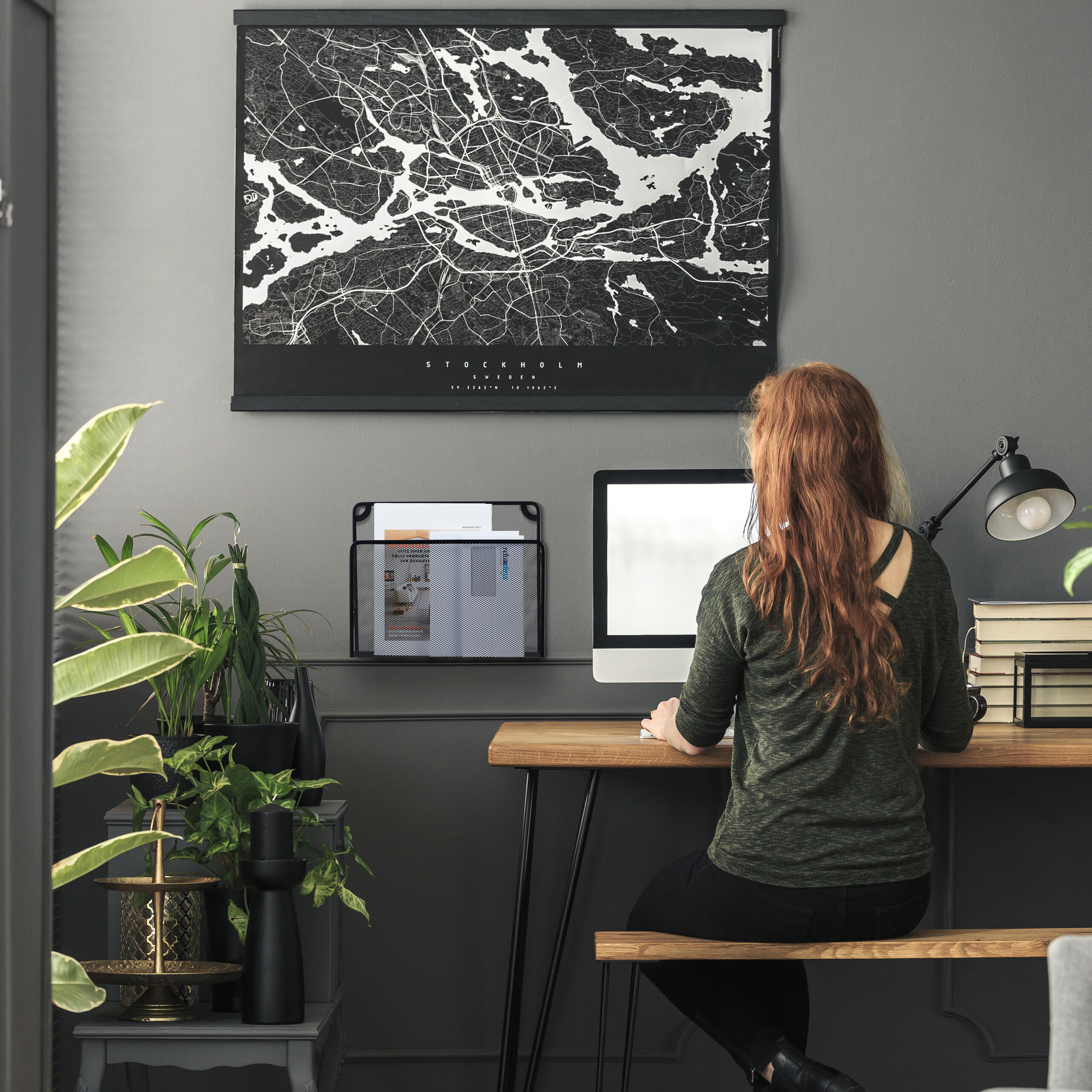 Eine Frau mit roten Haaren sitzt an einem Schreibtisch vor einem Computer, darüber hängt eine Stockholm-Karte.