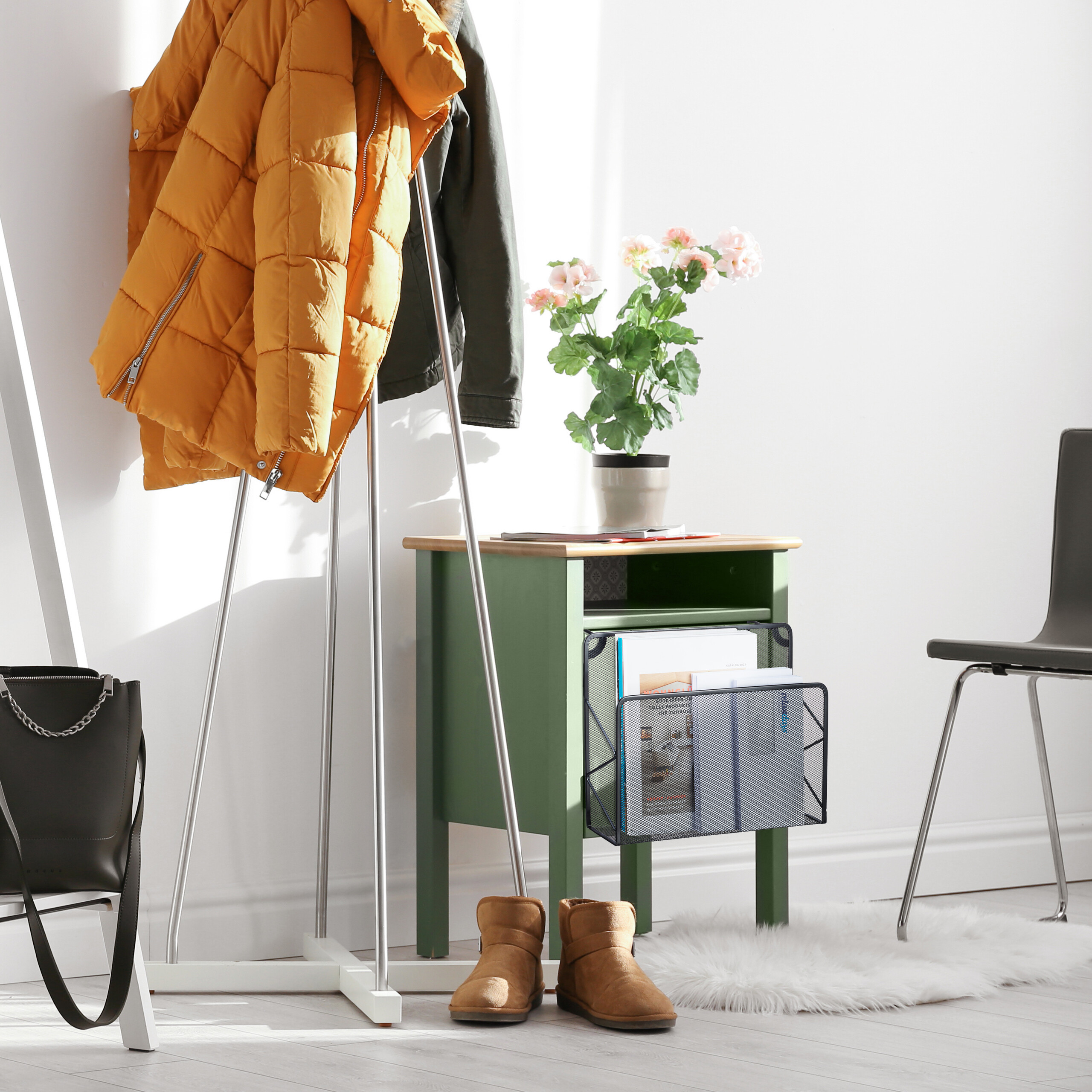 Ein heller Flur mit Garderobe, gelber Jacke, grünem Schränkchen mit Blumen und Stiefeln auf weißem Boden.