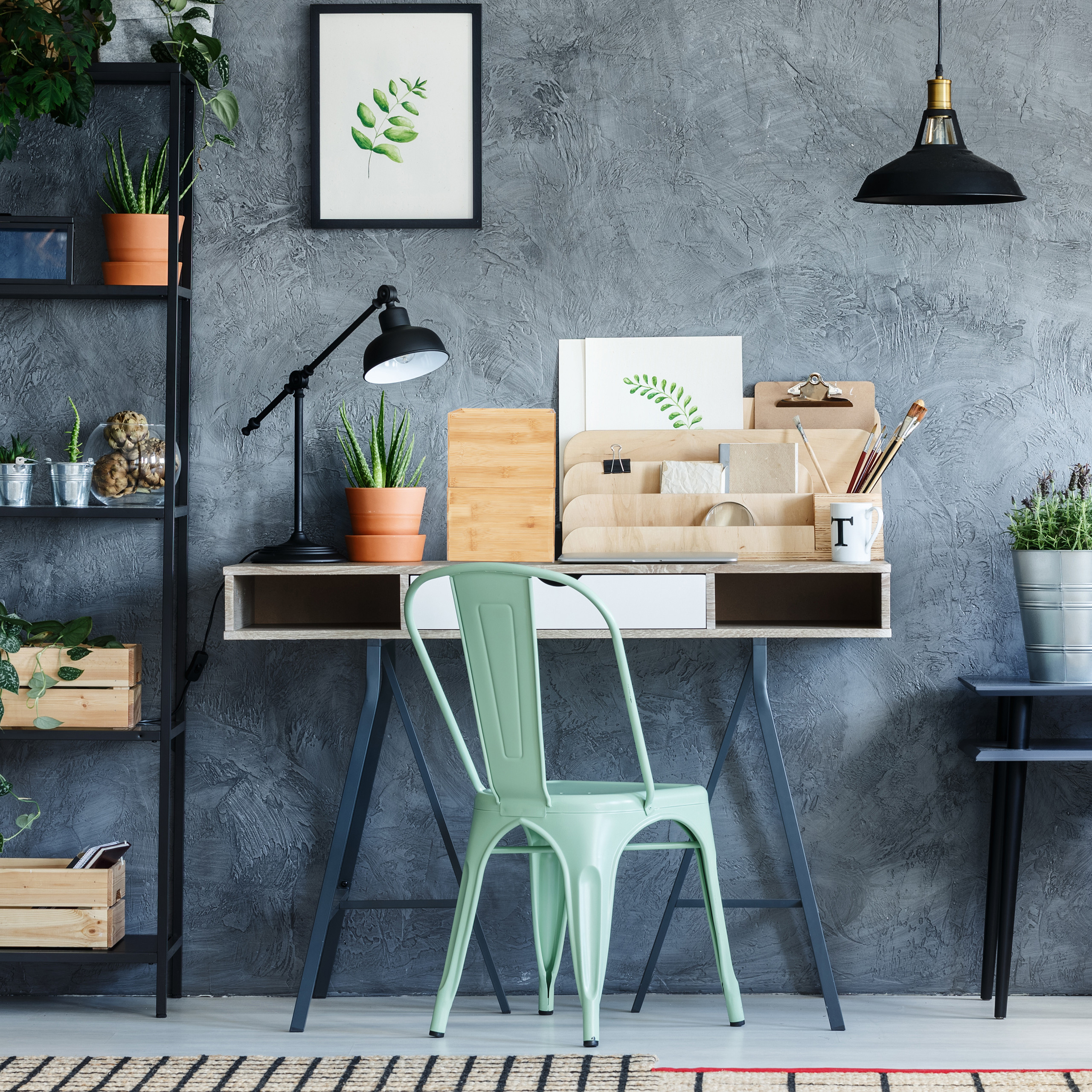 Ein heller Schreibtisch mit mintgrünem Stuhl, Pflanzen, Holzorganizer und einer grauen Wand im Hintergrund.