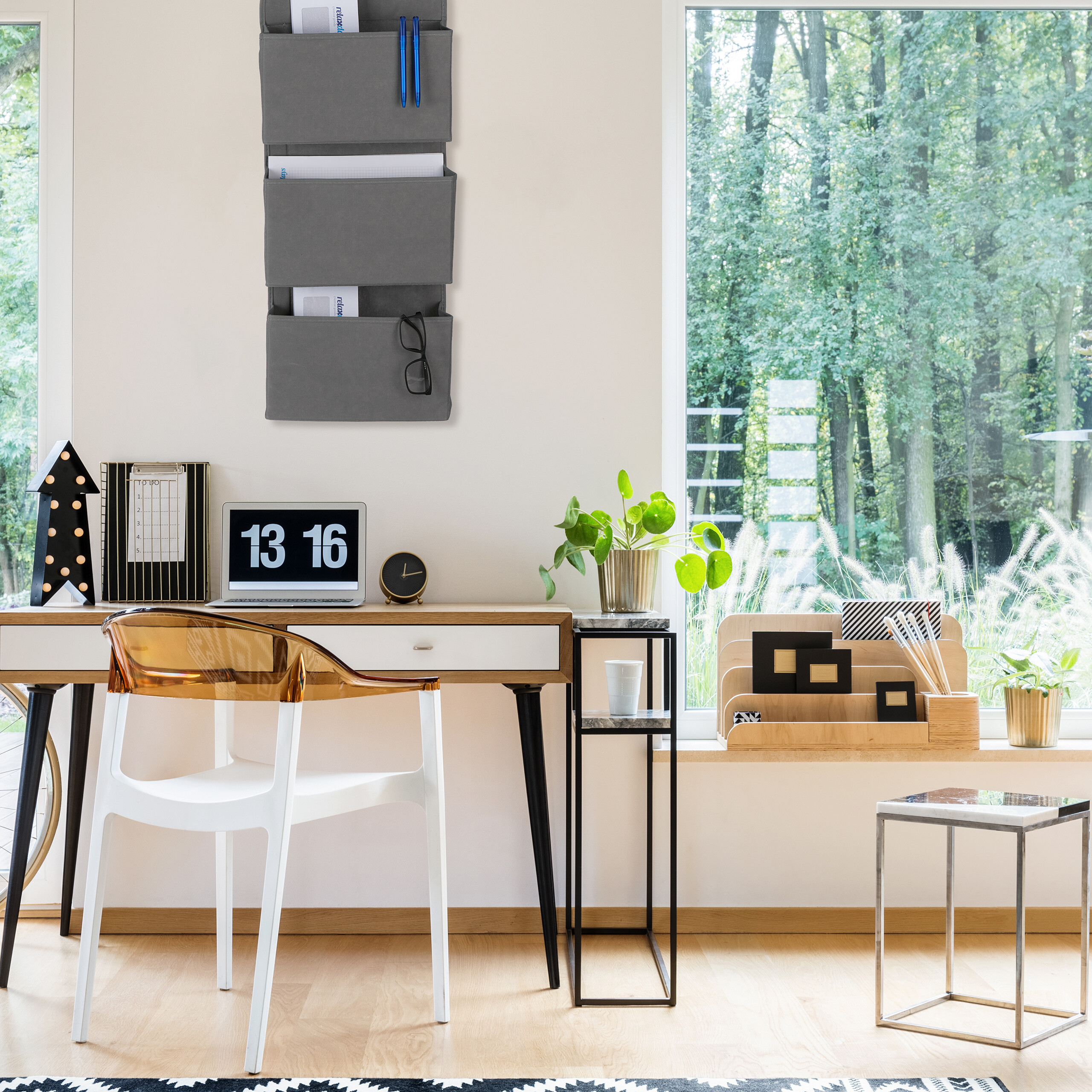 Ein modernes Homeoffice mit Holztisch, weißem Stuhl, grauem Wandorganizer und Blick auf den Wald durch das Fenster.