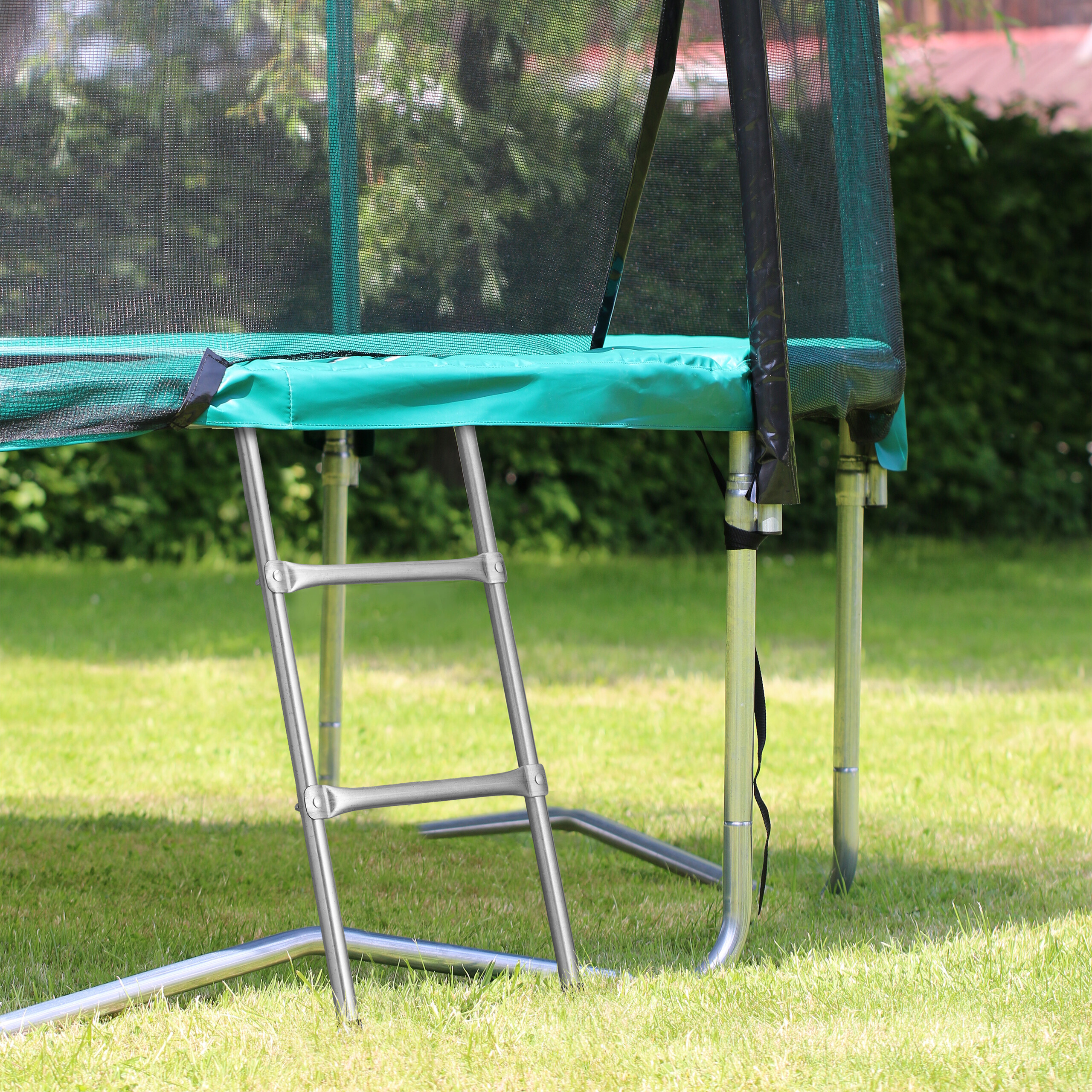 Ein Gartentrampolin mit grünem Rand, Sicherheitsnetz und einer kleinen Metallleiter im Garten.