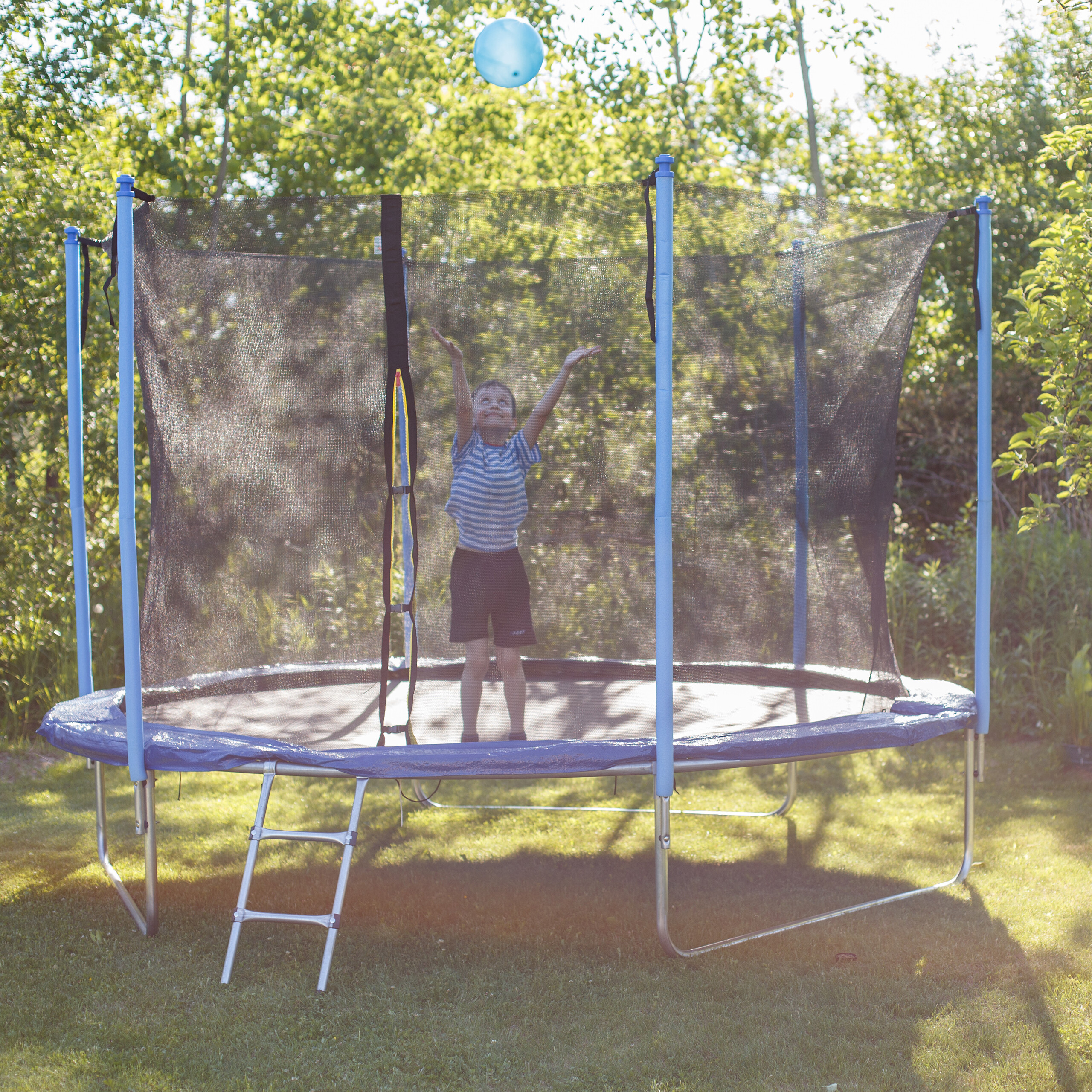 Ein Junge springt auf einem Gartentrampolin und fängt einen blauen Ball.