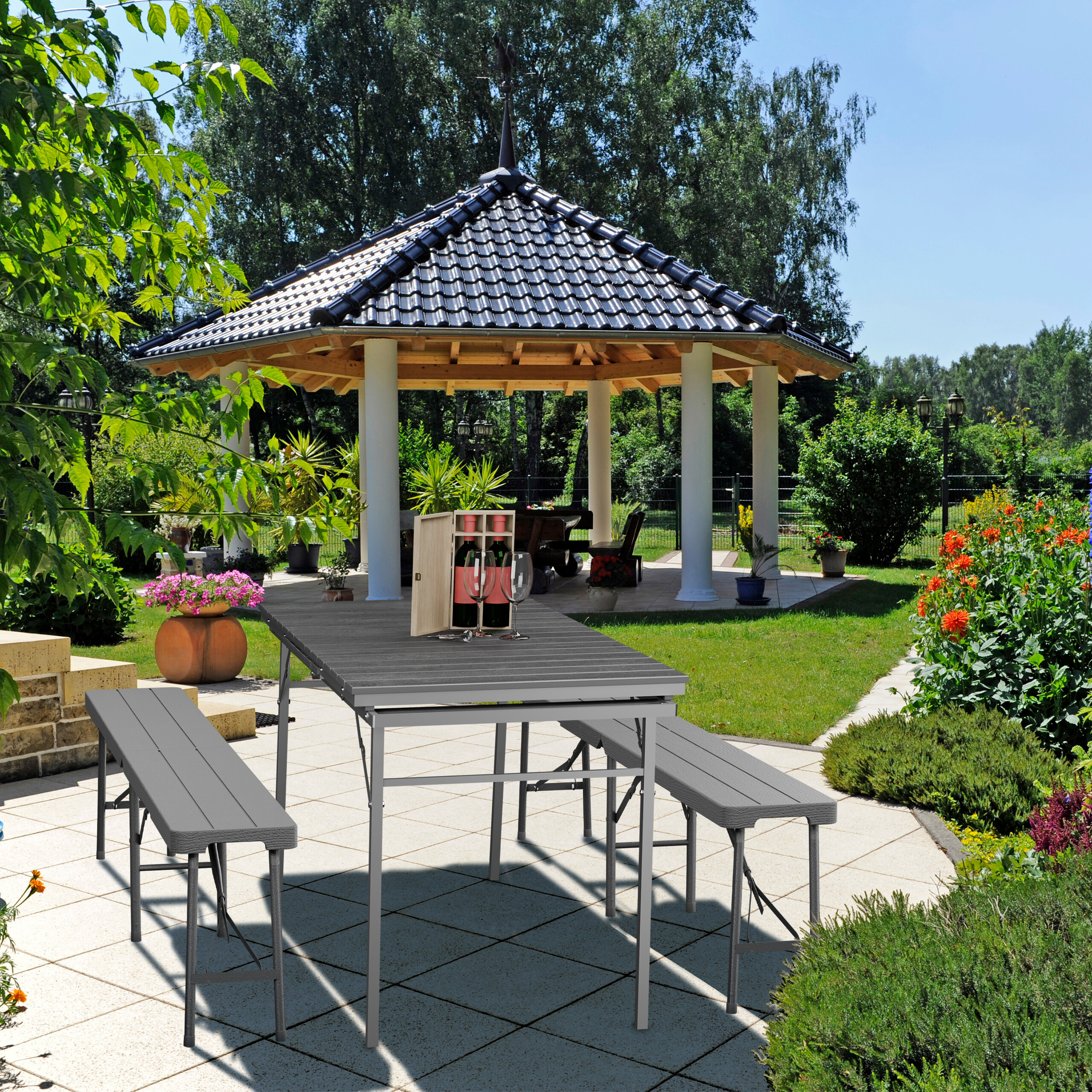 Grauer Gartentisch mit Bänken und Weinset auf gepflasterter Terrasse im Garten mit Pavillon.