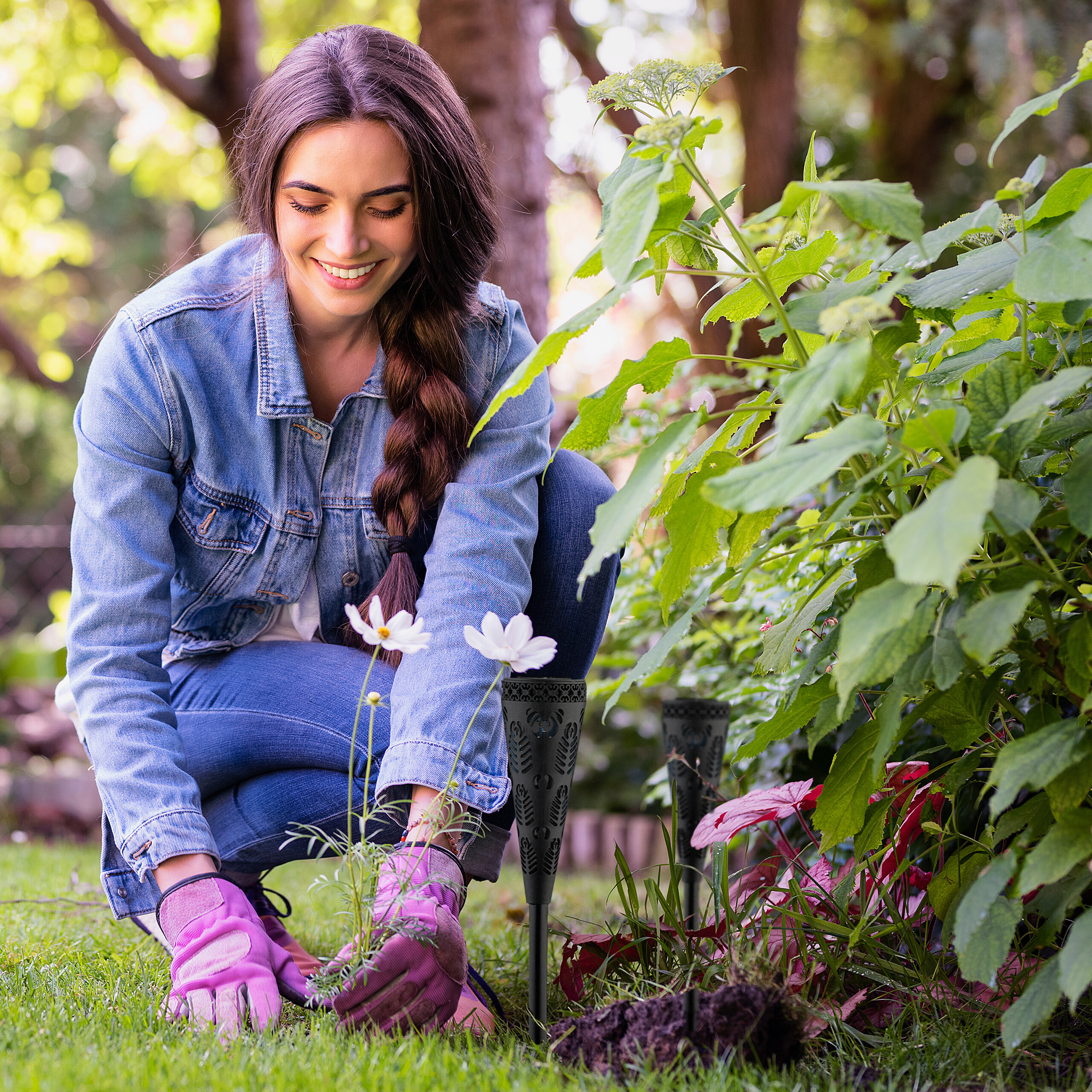 Eine Frau in Jeansjacke und rosa Handschuhen gärtnert im Freien und pflanzt kleine Blumen.