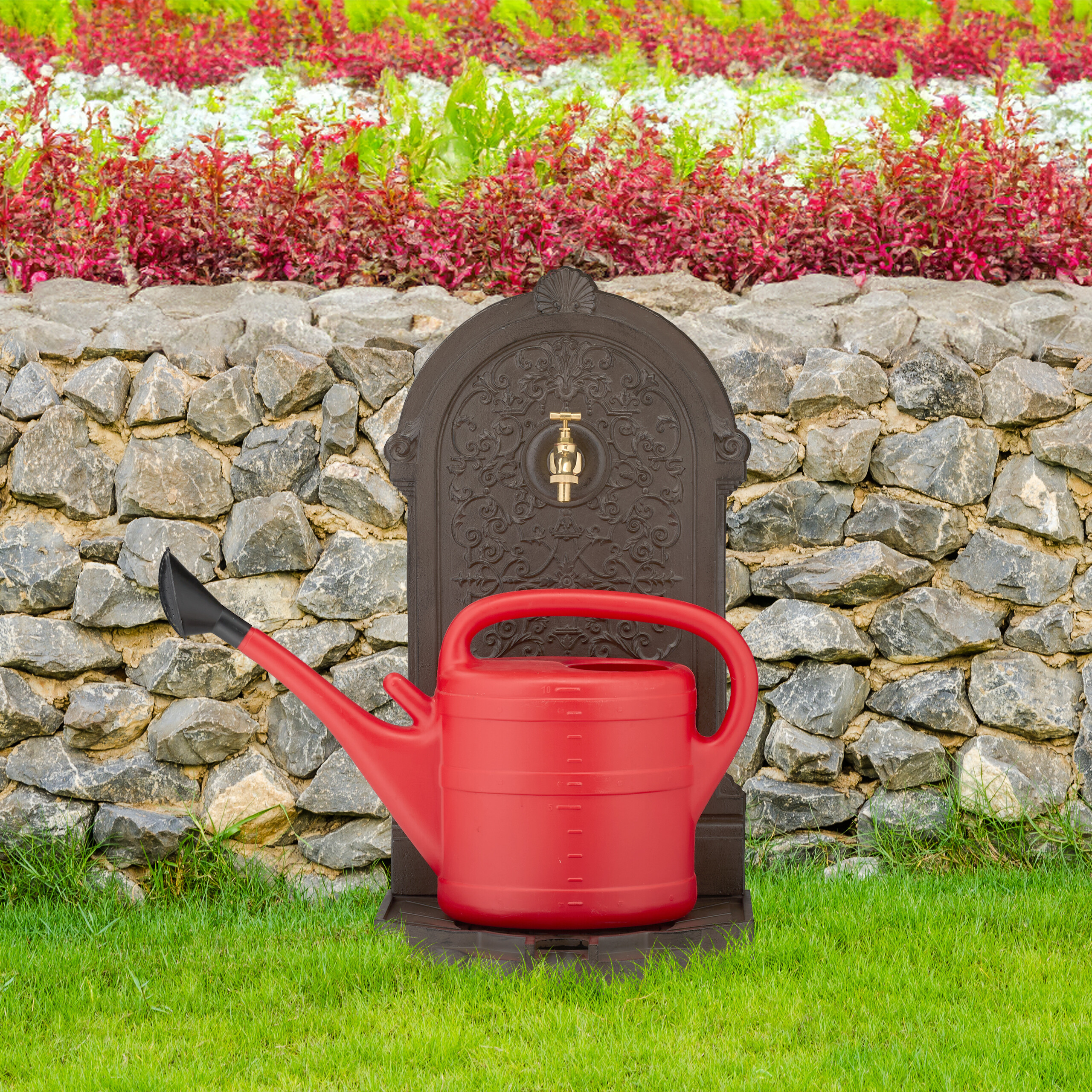 Eine rote Gießkanne vor einem dekorativen Brunnen und einer Steinmauer im Garten.