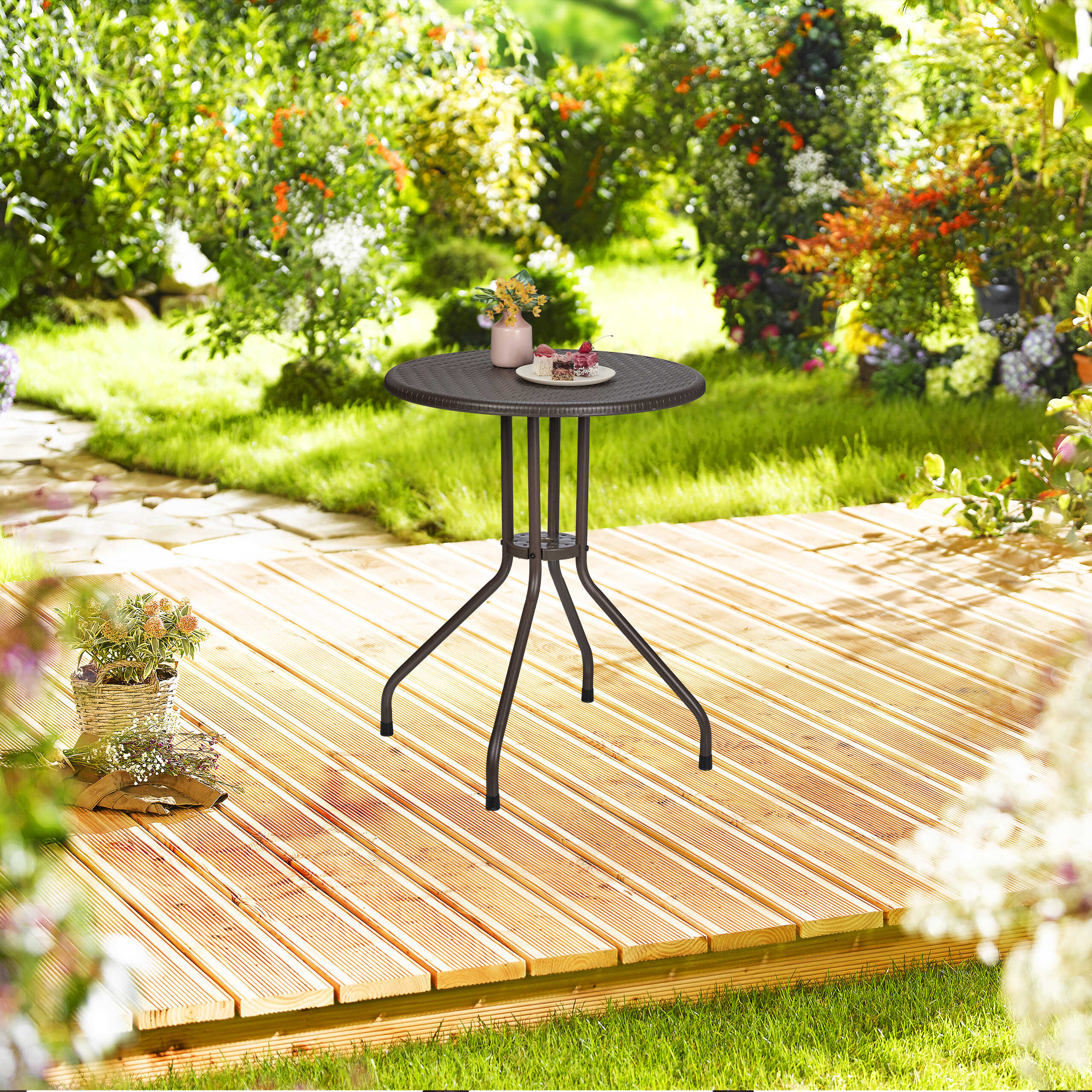 Kleiner runder Gartentisch mit Teller und Vase auf einer Holzterrasse im grünen Garten.