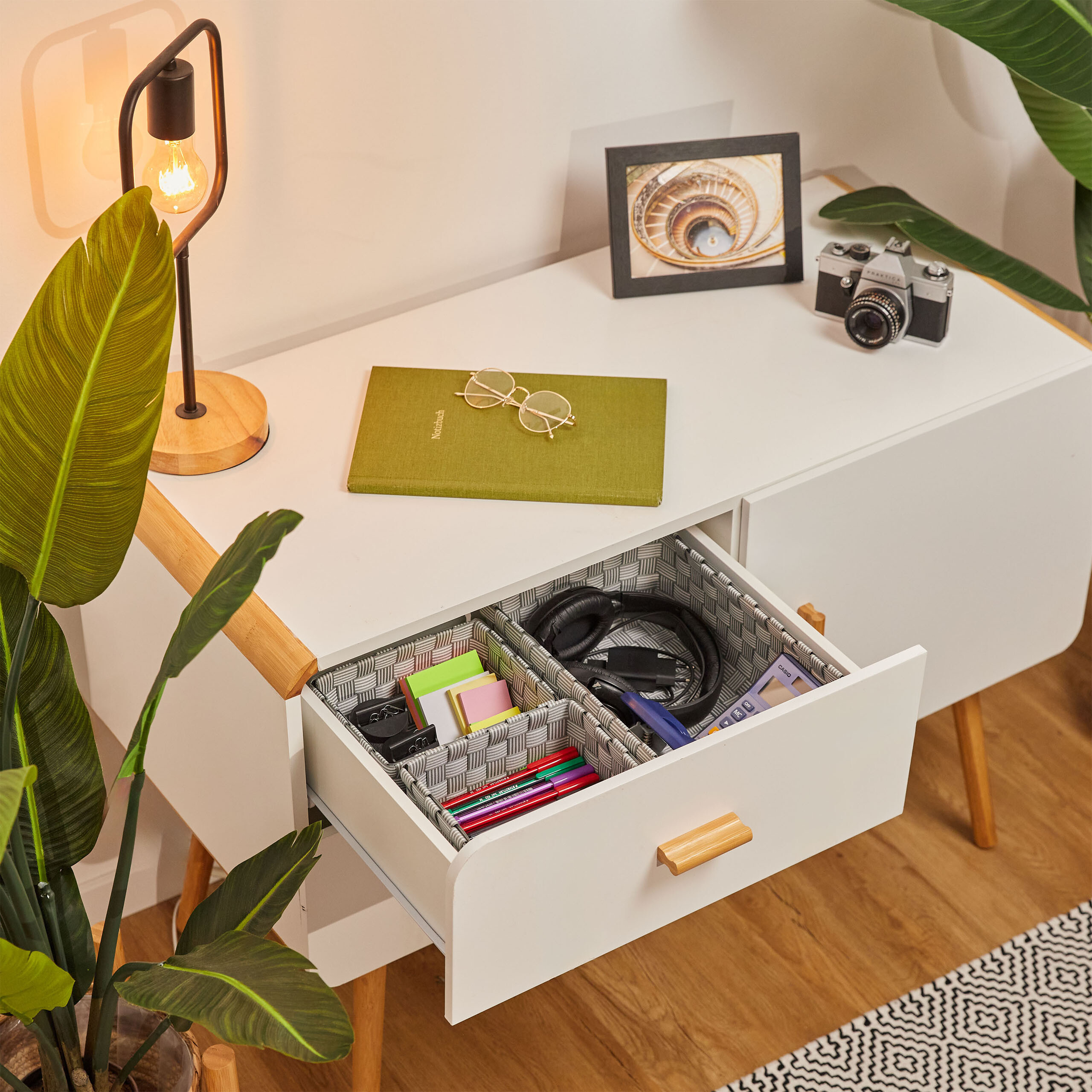 Ein weißer Schrank mit geöffneter Schublade, die Organizer mit Stiften, Haftnotizen, Kopfhörern und Rechner zeigt.