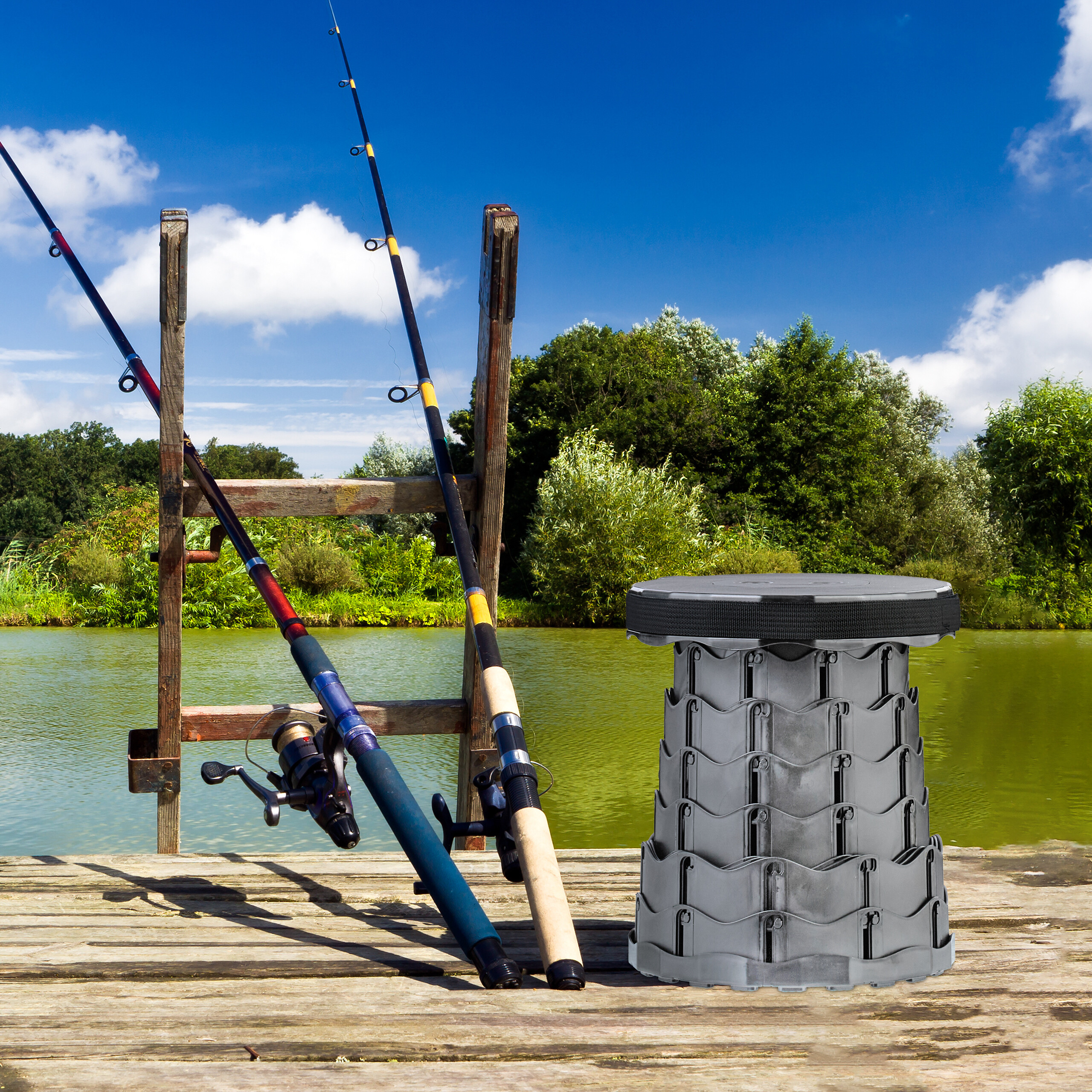 Zwei Angelruten lehnen an einem Holzsteg mit Klapphocker vor See und blauem Himmel.