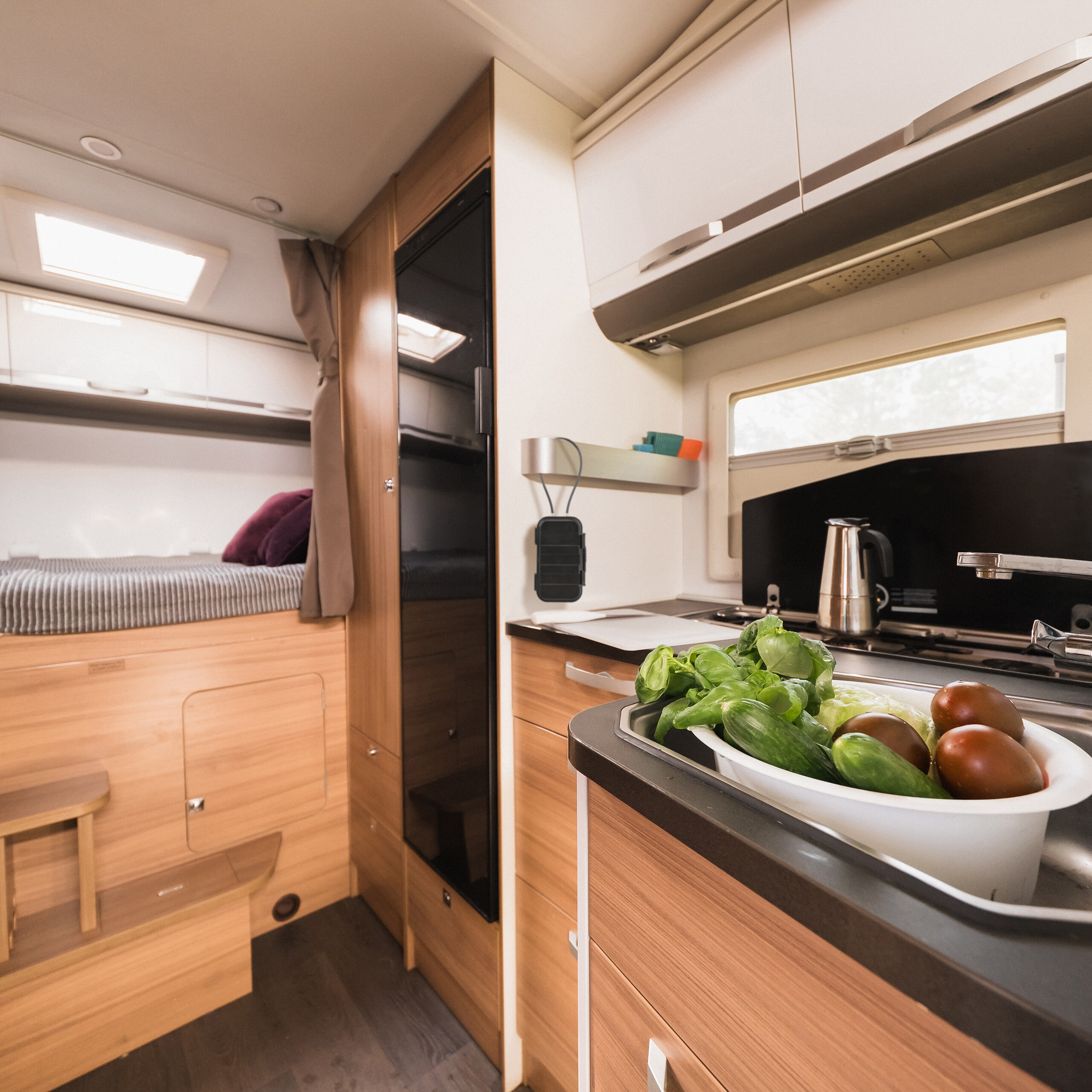 Wohnmobil-Innenraum mit Küche im Vordergrund mit Gemüse im Waschbecken und einem Bett im Hintergrund links.