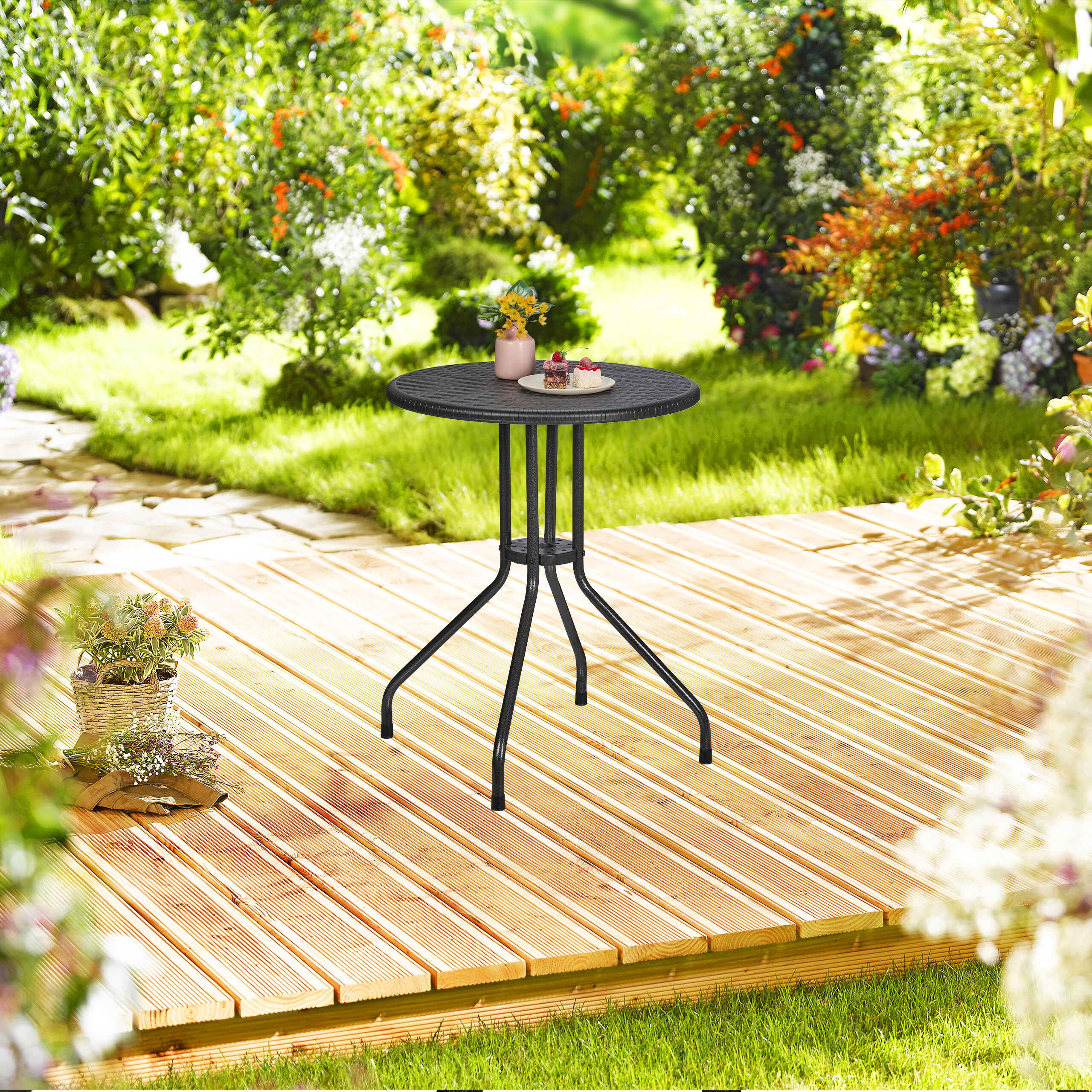 Ein schwarzer runder Gartentisch auf einem Holzdeck, umgeben von üppigem Grün und Blumen.