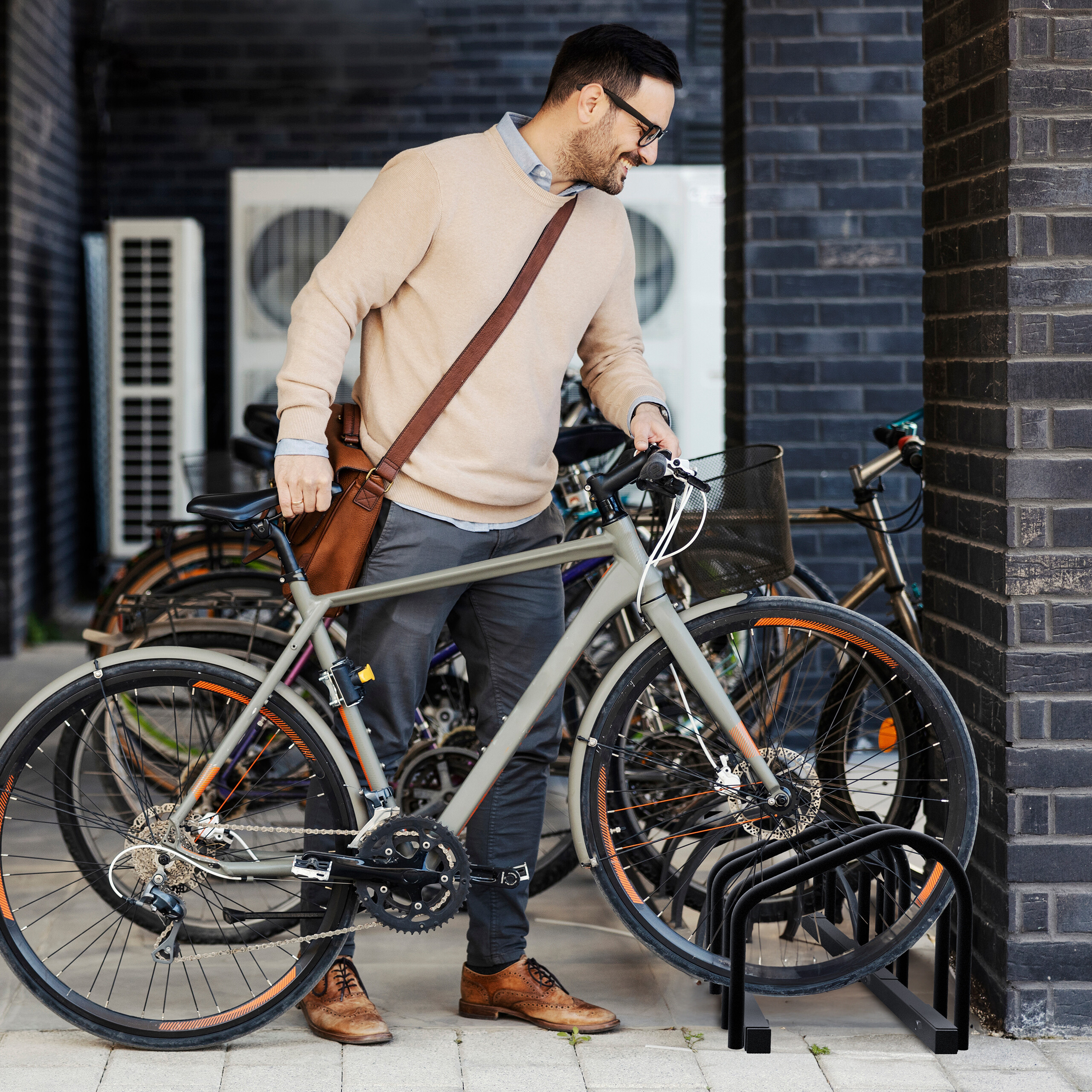 Ein lächelnder Mann im beige Pullover holt ein graues Fahrrad aus einem Fahrradständer.