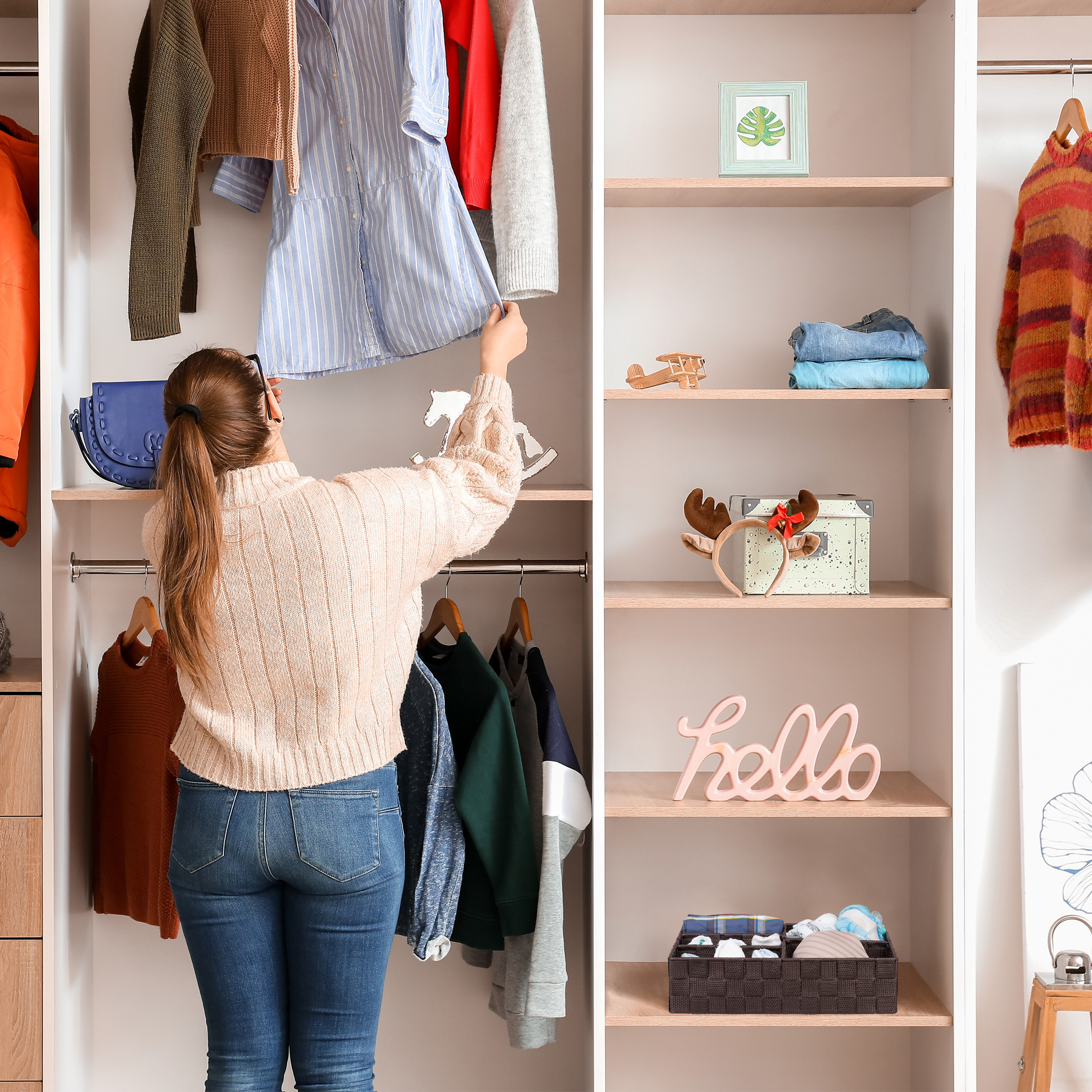 Eine Frau in einem Pullover wählt Kleidung aus einem großen, organisierten Kleiderschrank aus.