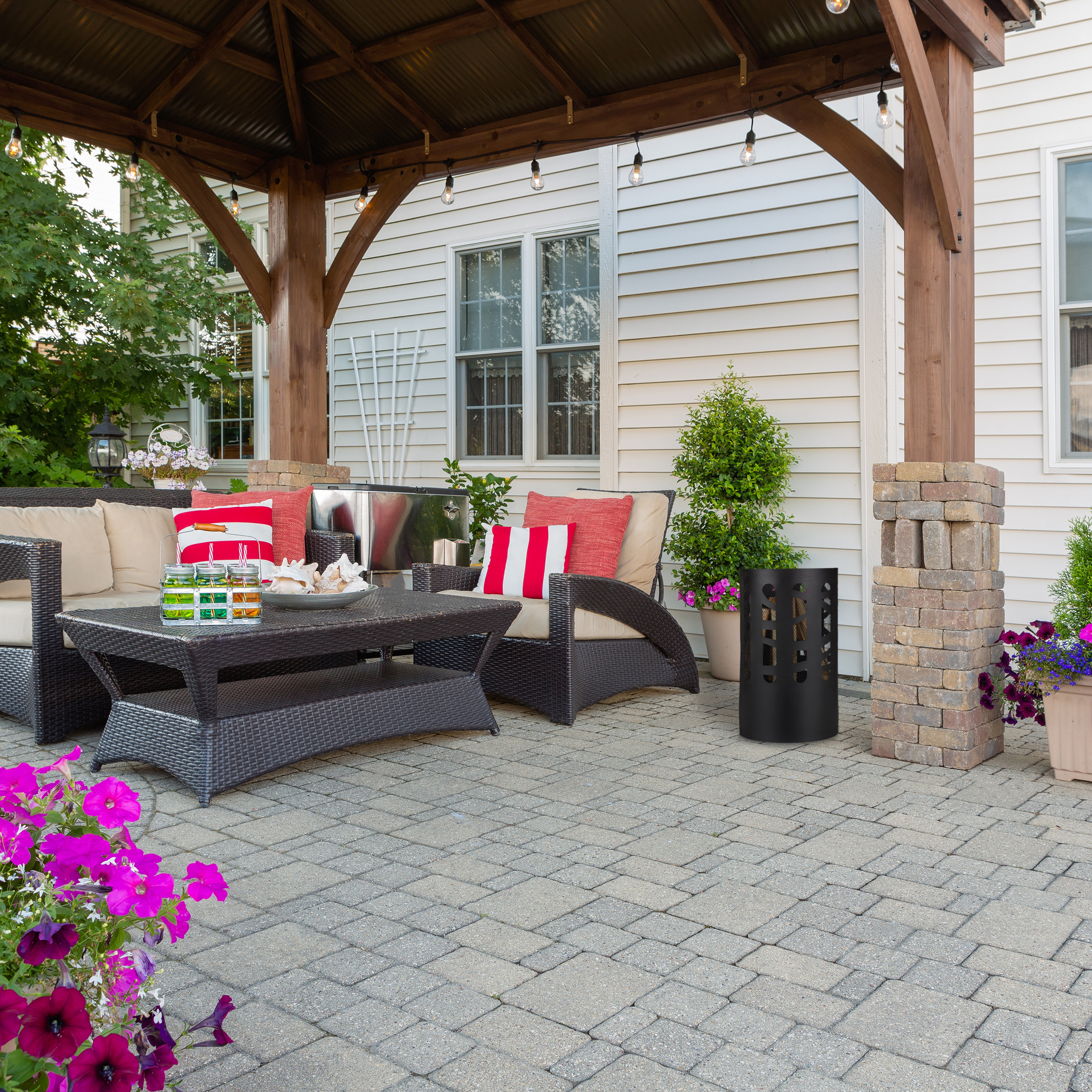 Gemütliche Terrasse mit Holzdach, Rattanmöbeln, roten Kissen, Getränken auf dem Tisch und Blumentöpfen.