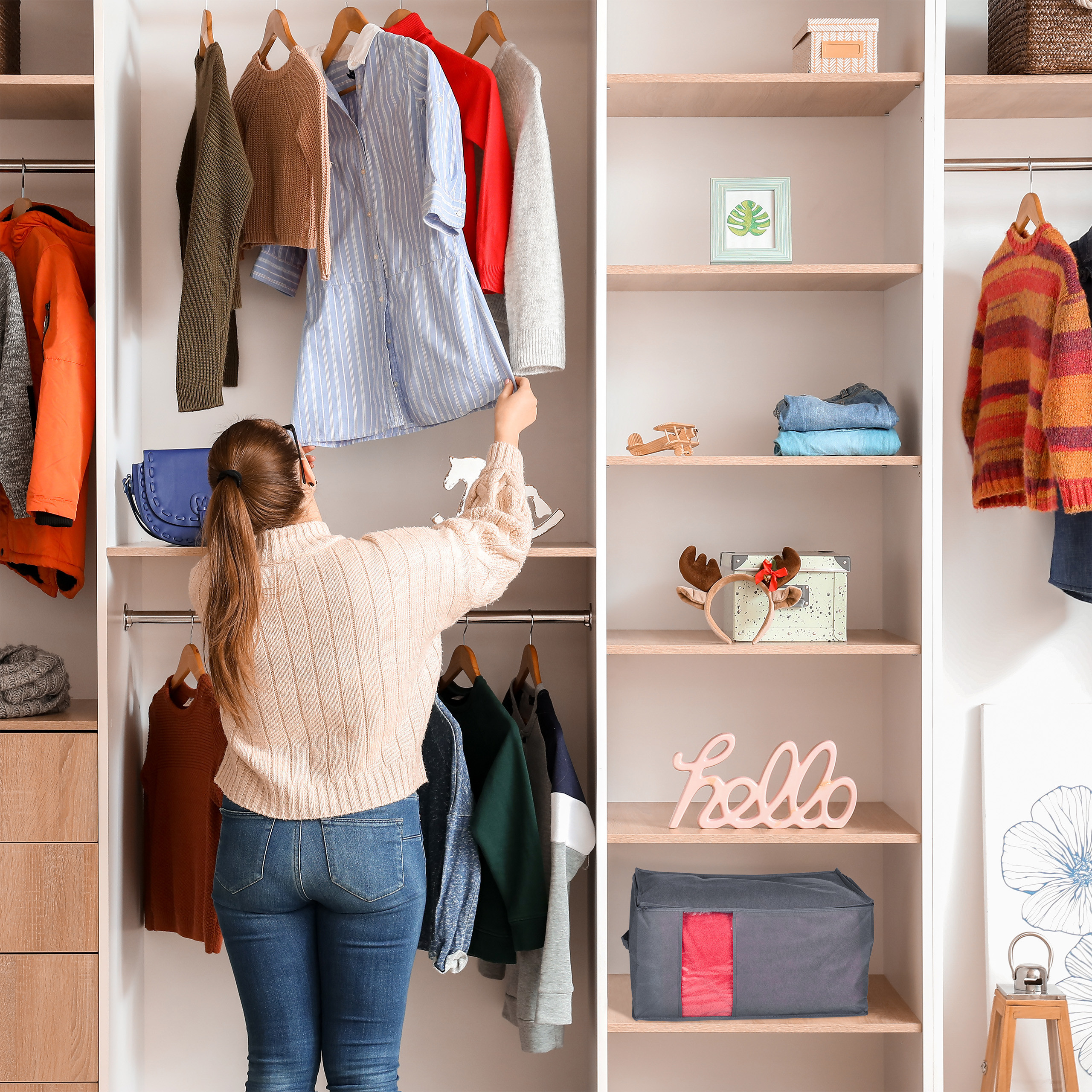 Eine Frau in einem Pullover und Jeans wählt Kleidung aus einem großen, organisierten Kleiderschrank aus.