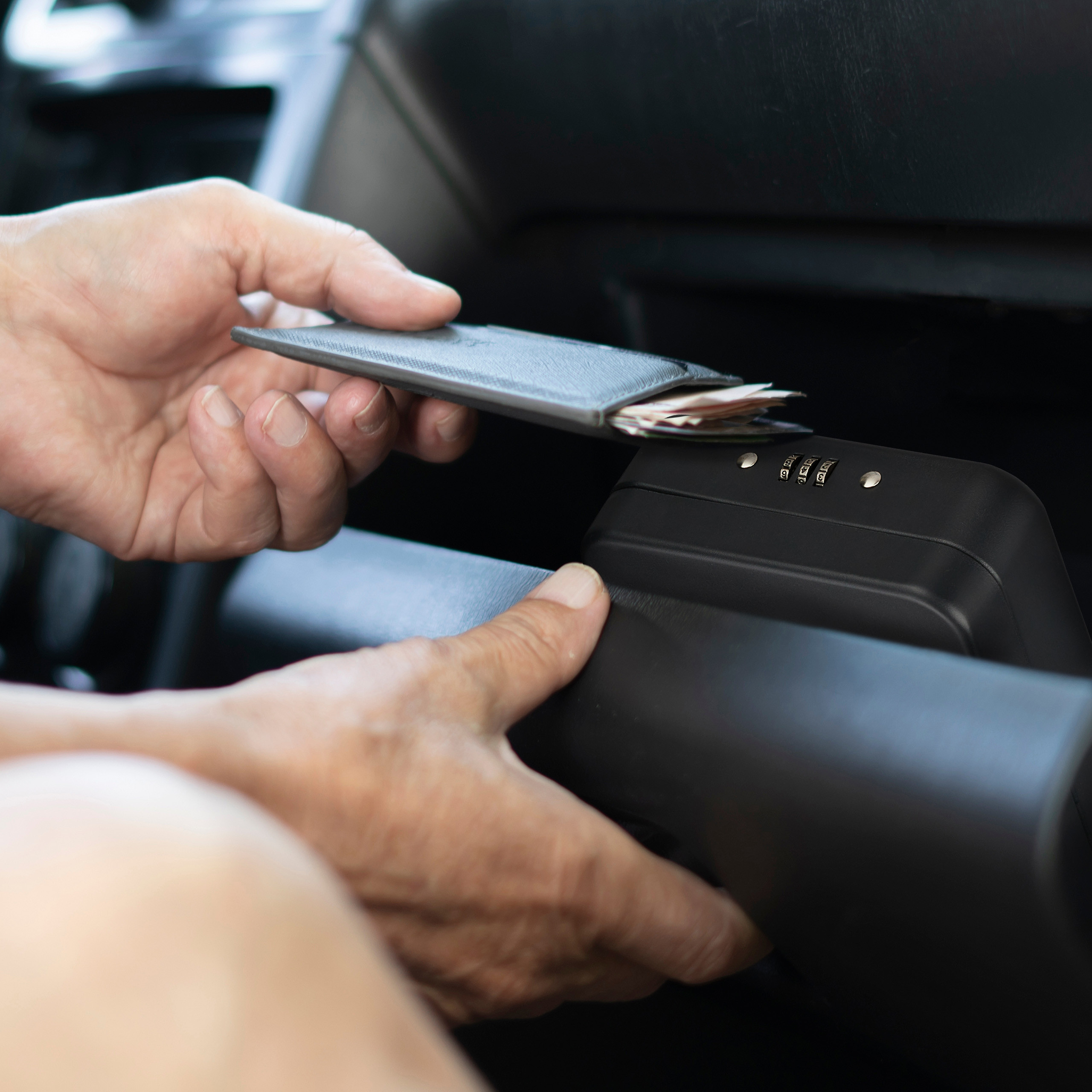 Eine Person legt eine Brieftasche mit Geld in eine tragbare Autotresor mit Zahlenschloss.