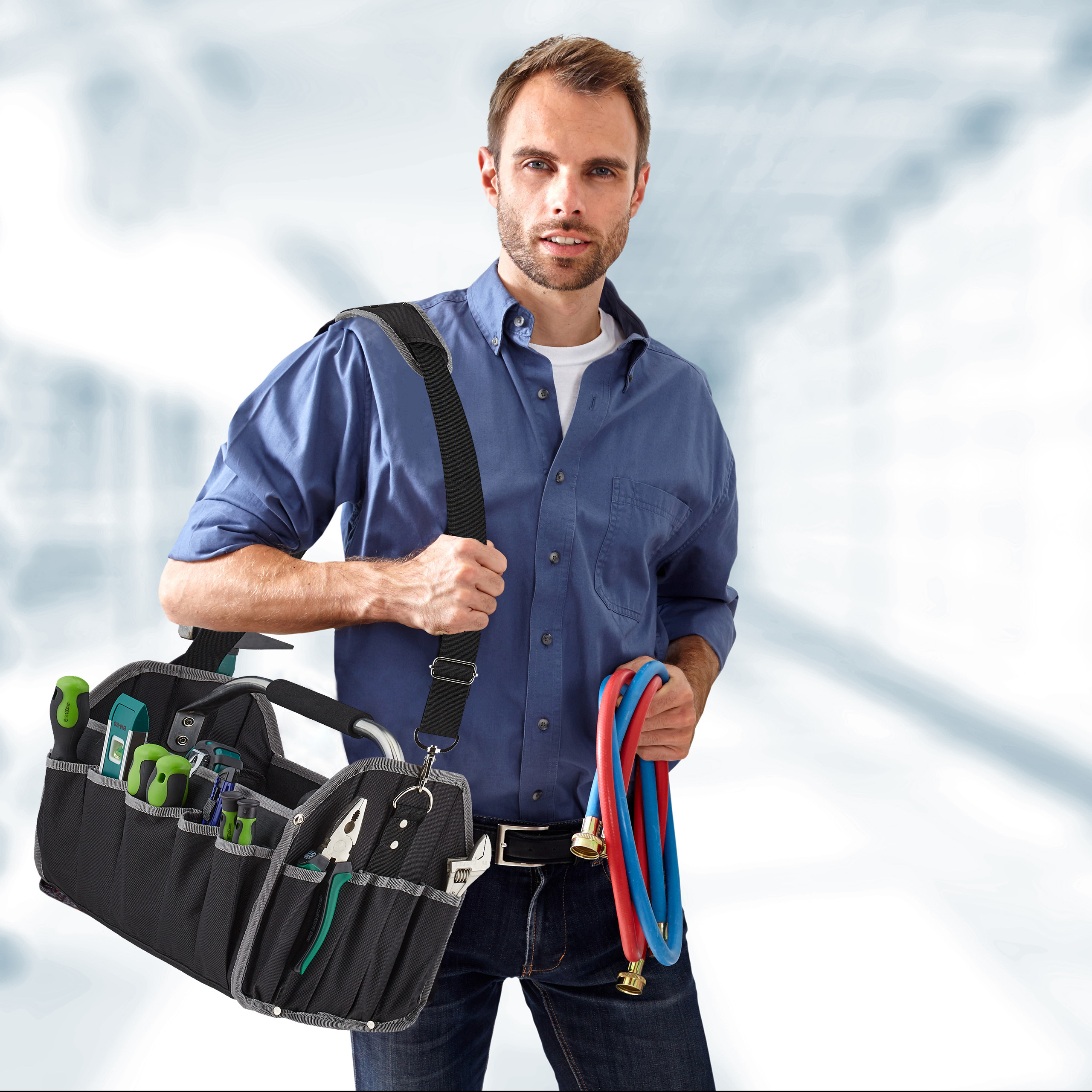 Ein Handwerker mit blauem Hemd trägt eine Werkzeugtasche und Rohre.