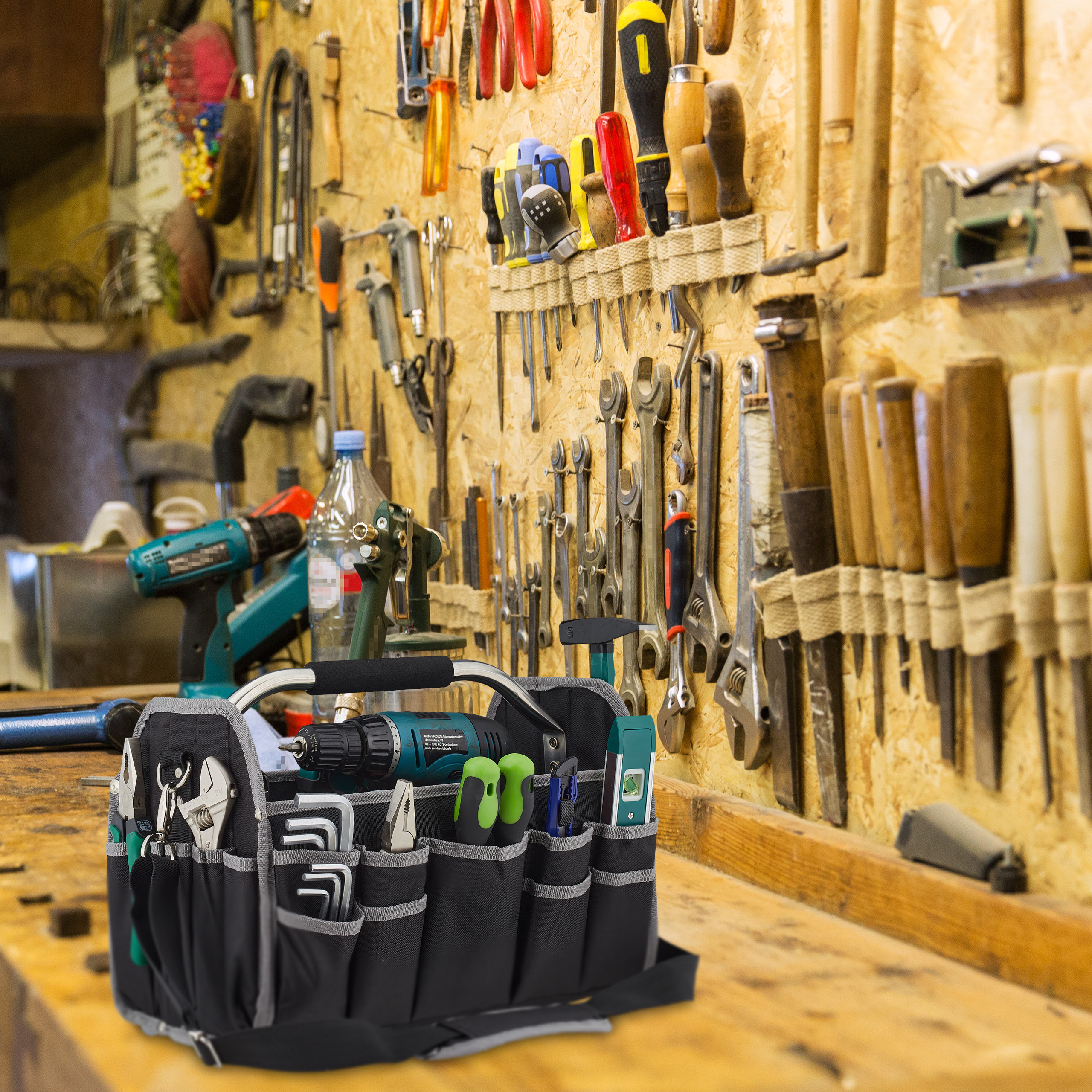Eine Werkzeugtasche mit Akku-Schrauber und Handwerkzeugen steht auf einer Holzwerkbank vor einer Werkzeugwand.