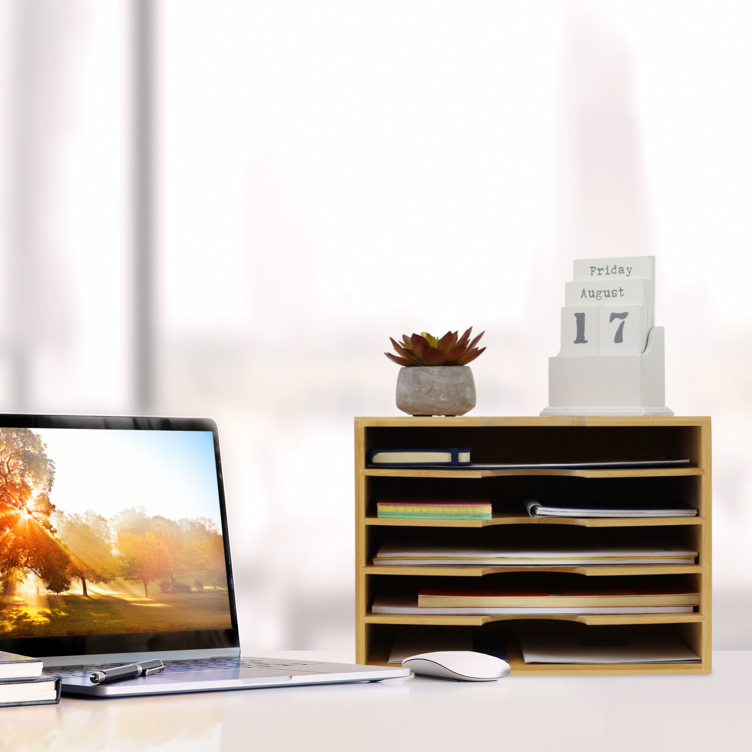 Ein Schreibtisch mit Laptop, Stift, Holzkiste mit Notizen, Pflanze und Kalender.