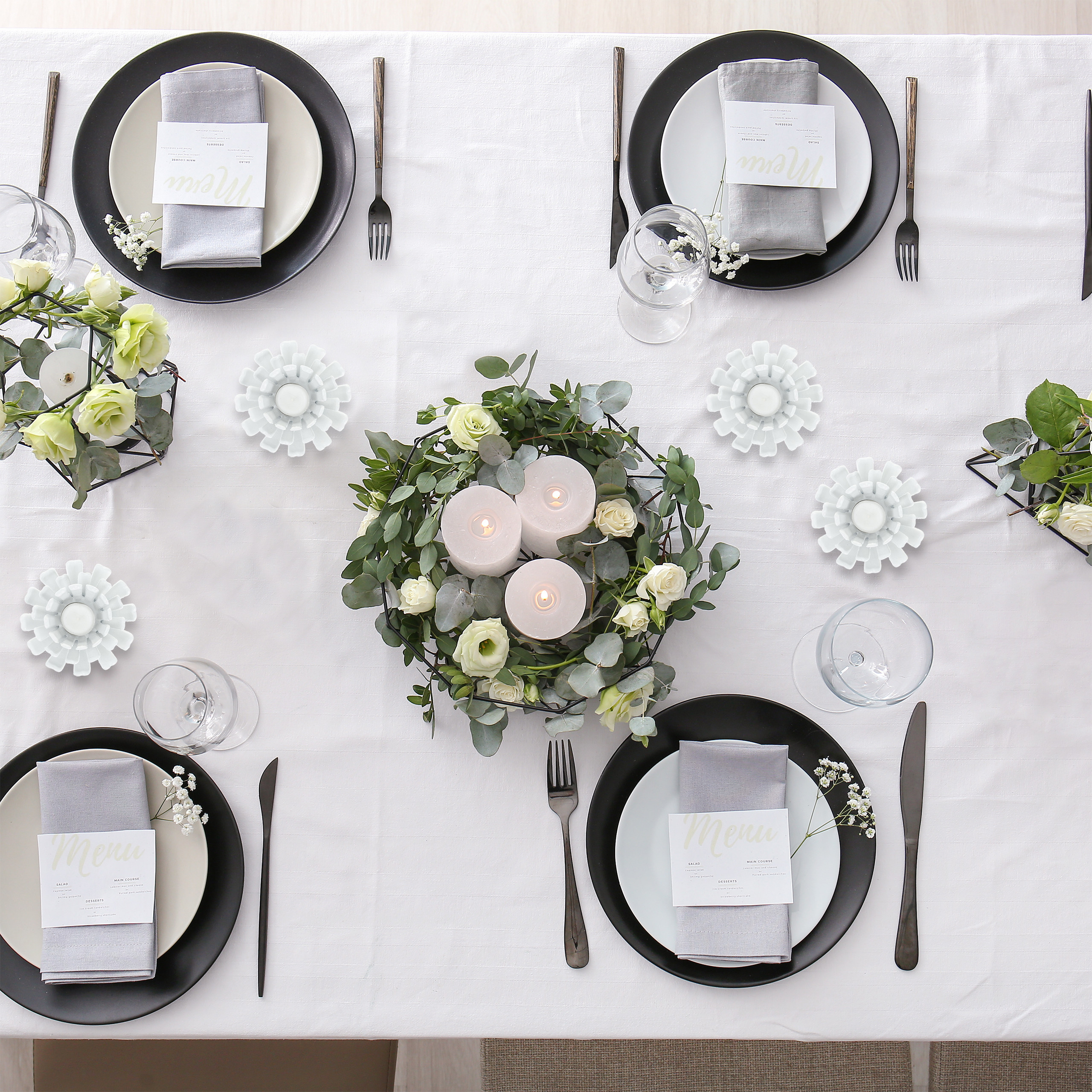 Ein formell gedeckter Esstisch mit vier Gedecken, weißen Tellern, grauen Servietten und Blumenarrangements.