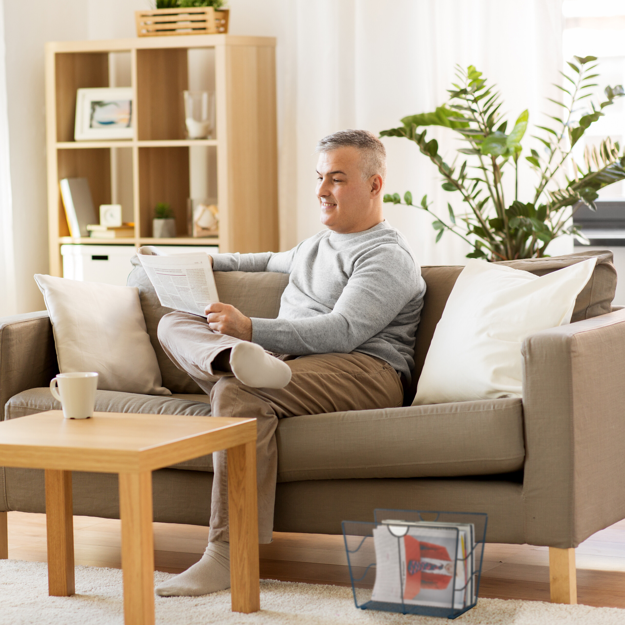 Ein Mann sitzt entspannt auf einem Sofa in einem hellen Wohnzimmer und liest eine Zeitung.