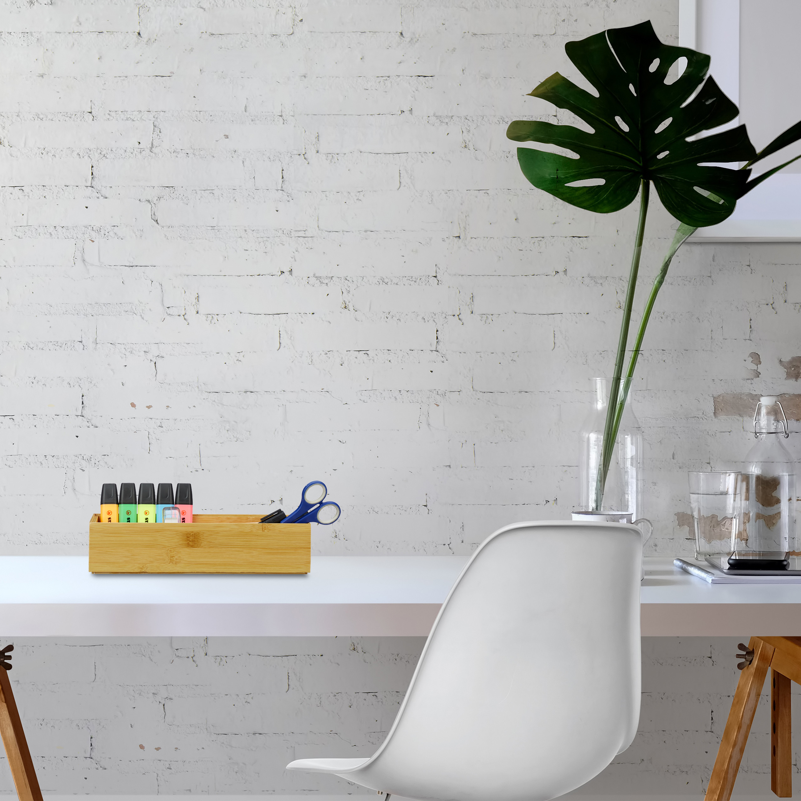 Ein weißer Schreibtisch mit Holzorganizer, Markern, Schere, Pflanze in Vase und weißem Stuhl.