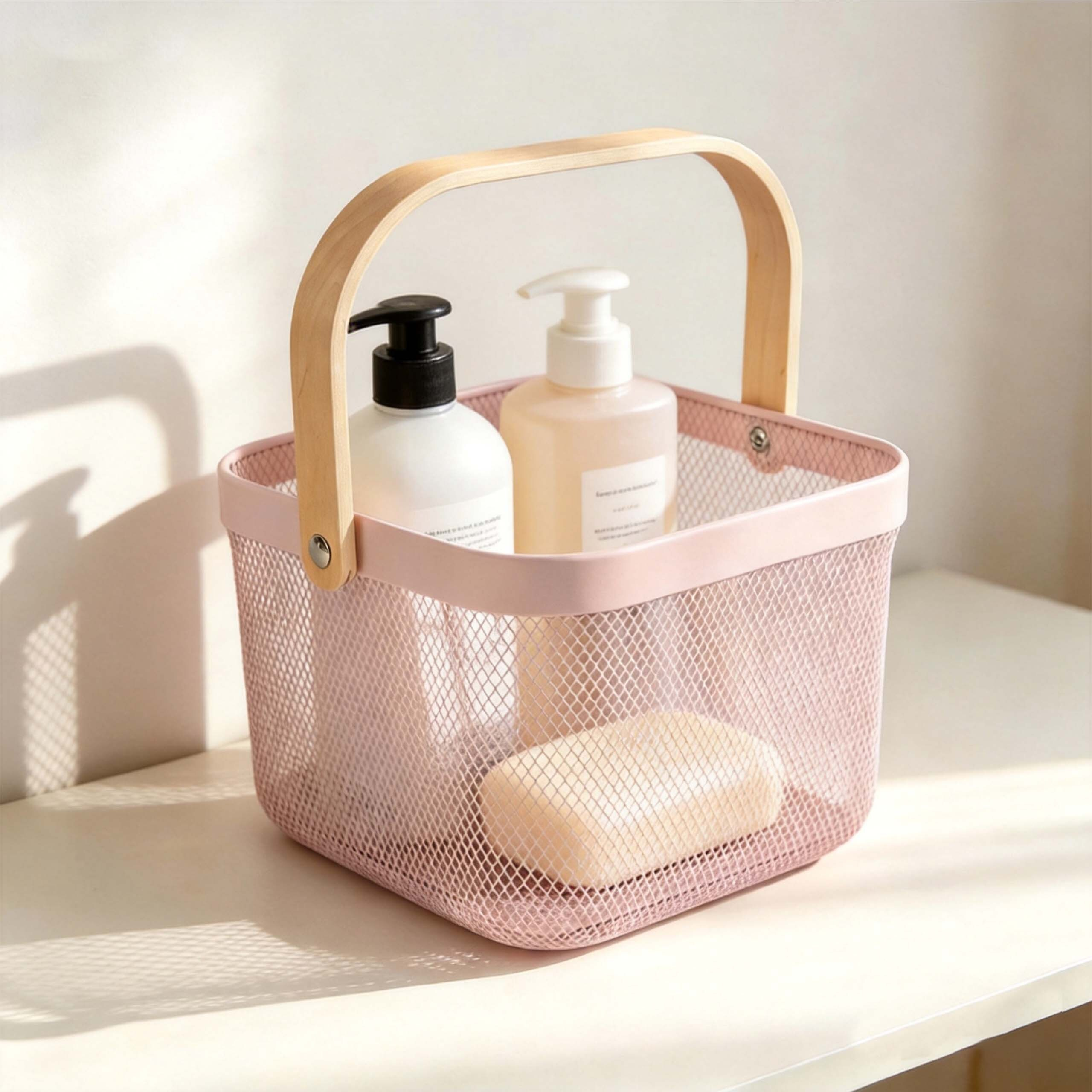 Ein rosa Drahtkorb mit Holzgriff auf weißer Fläche, gefüllt mit zwei Pumpflaschen und Seife.