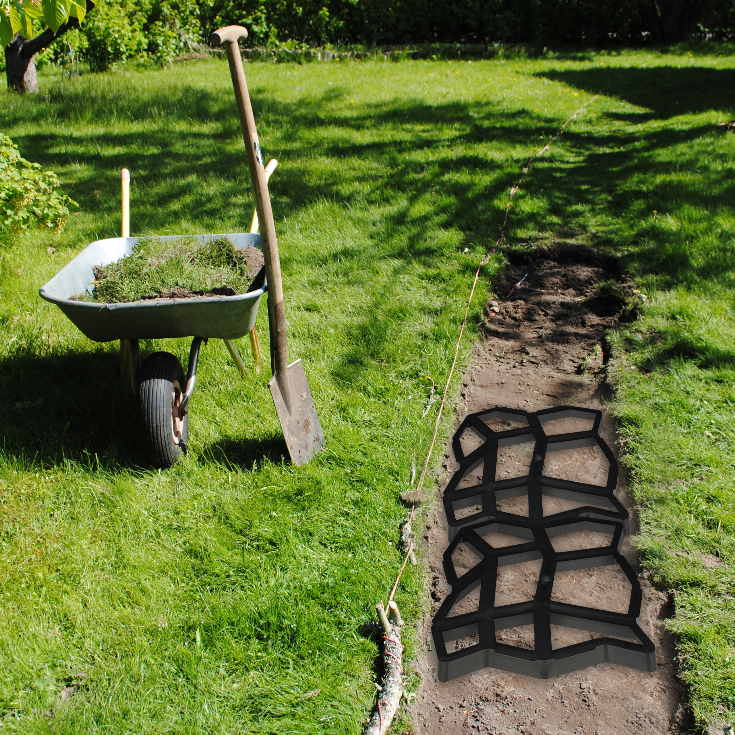 Eine Schubkarre mit Gras, eine Schaufel und eine Wegform im Garten.