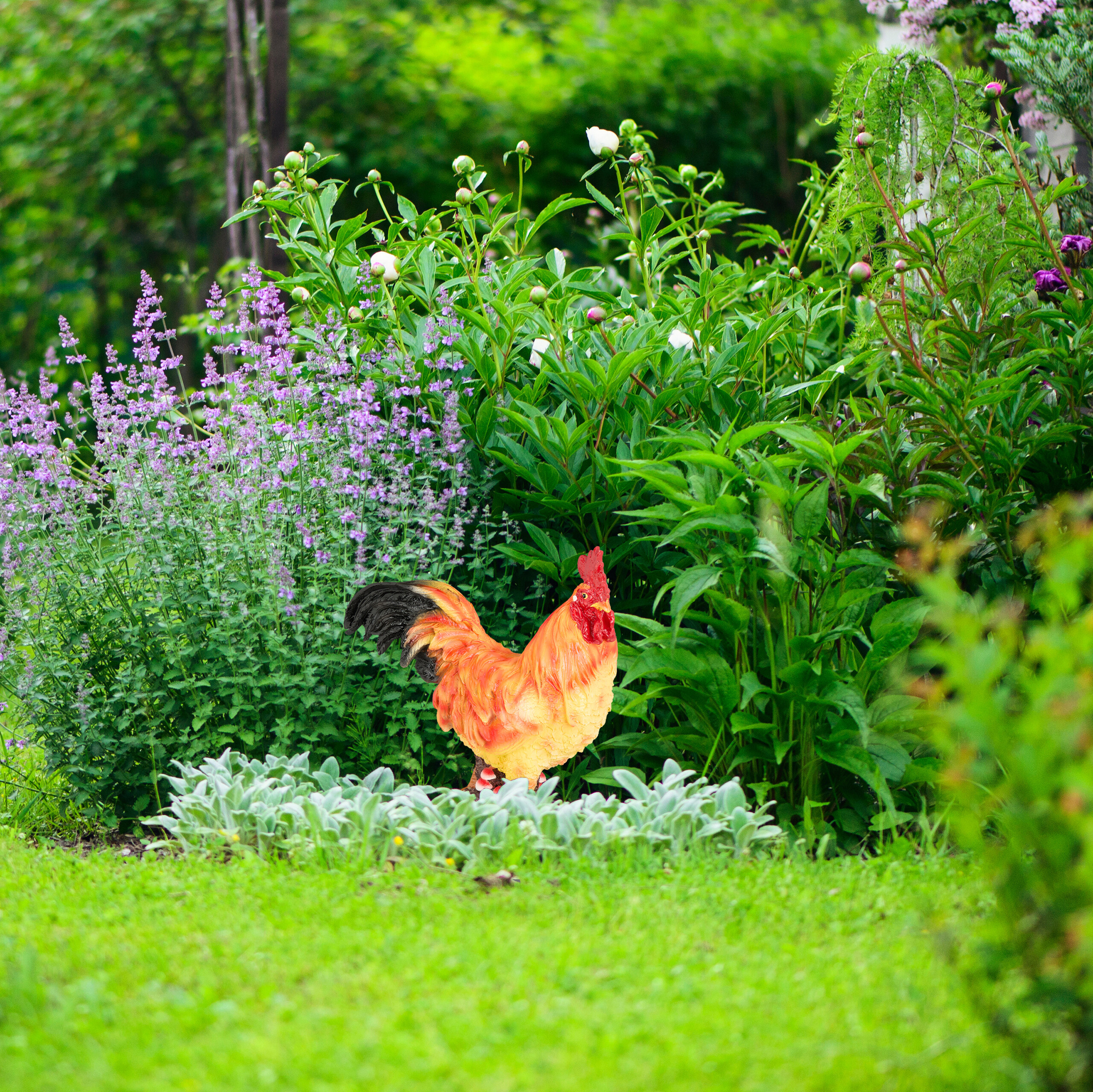 Eine bunte Hahnenstatue steht im Garten vor grünen Pflanzen und violetten Blumen.
