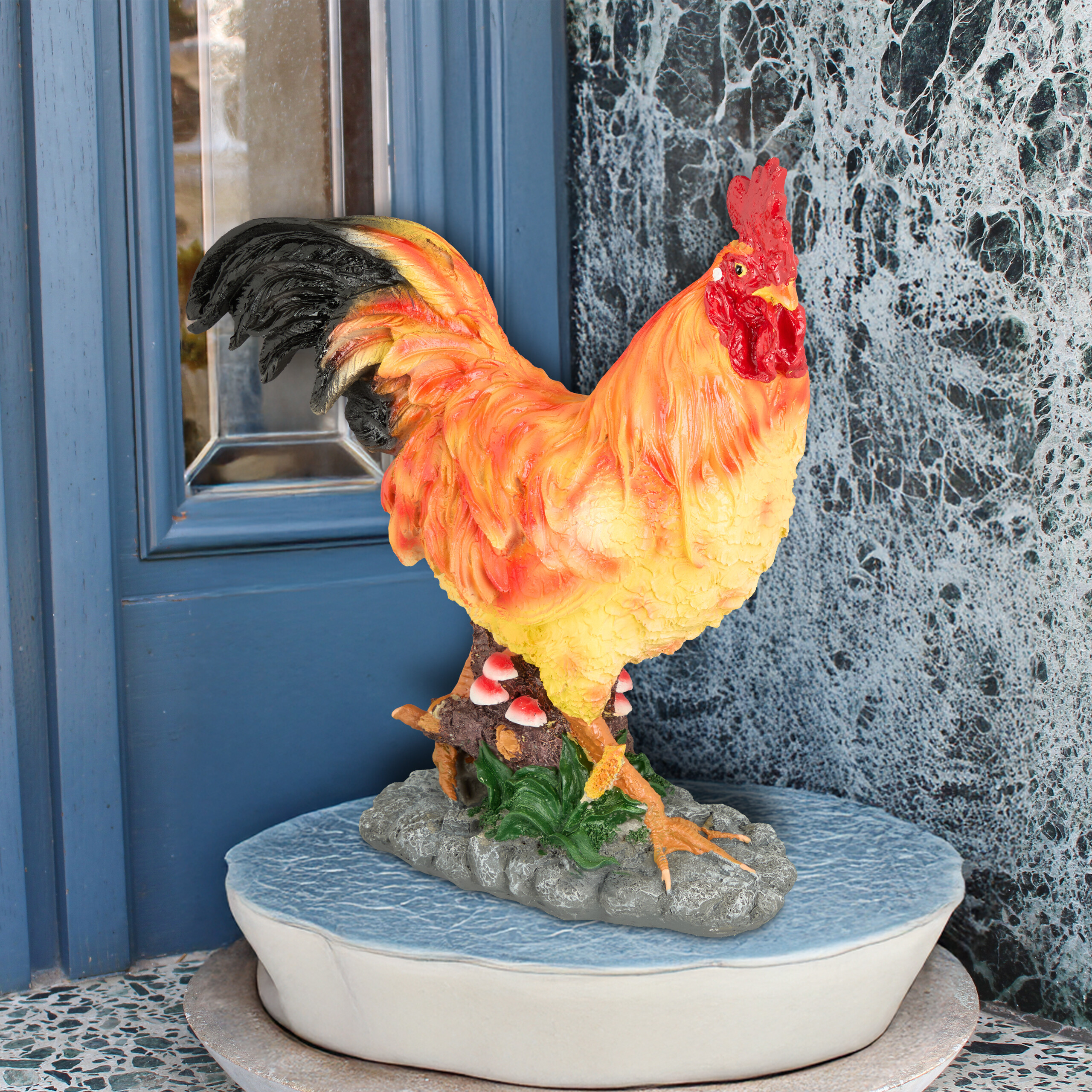 Eine bunte Hahnstatue mit rotem Kamm steht auf einem Festsockel vor blauer Tür und Marmorwand.