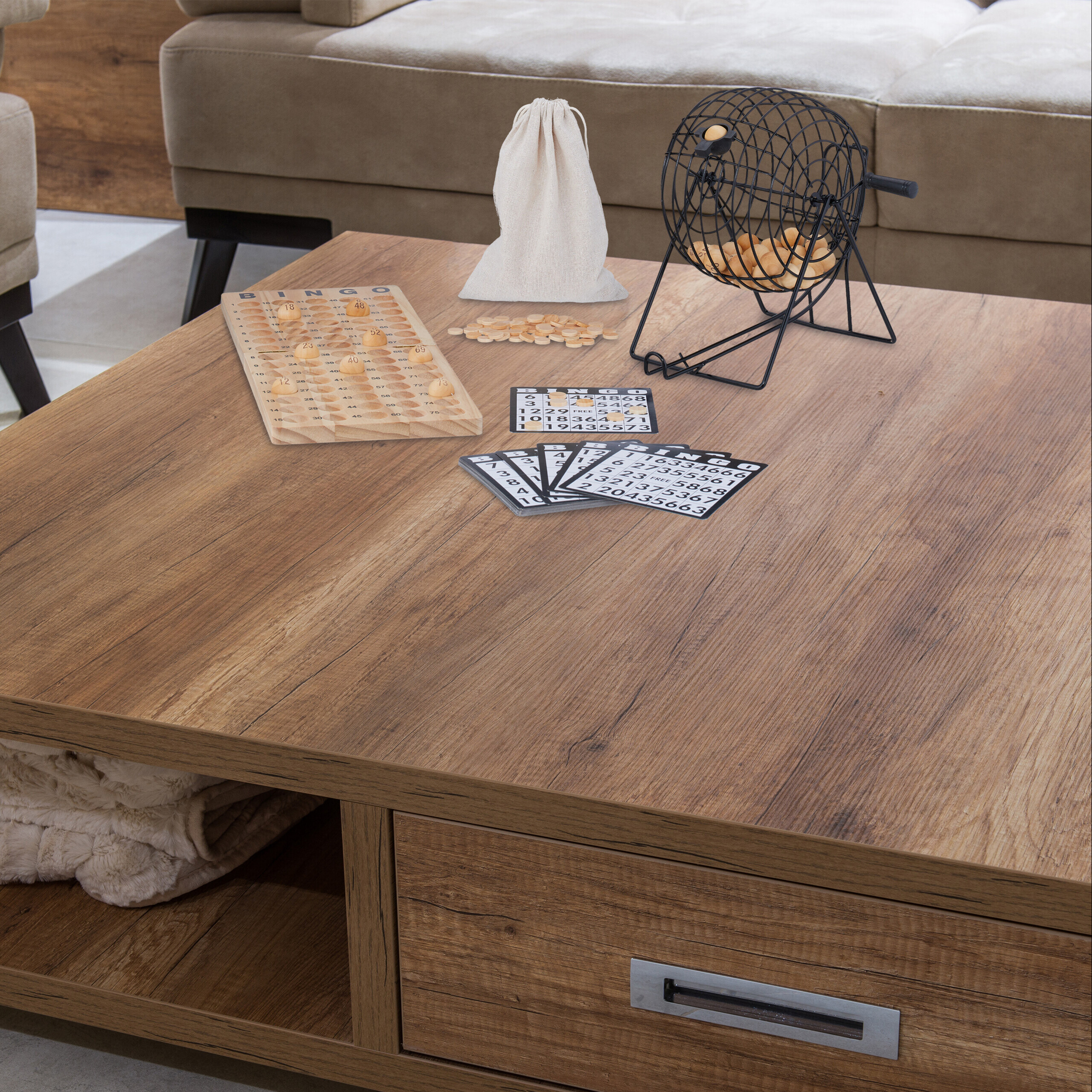 Ein Holztisch mit Bingospiel, Bällen im Metallkäfig, Karten und Beutel, im Hintergrund ein Sofa.