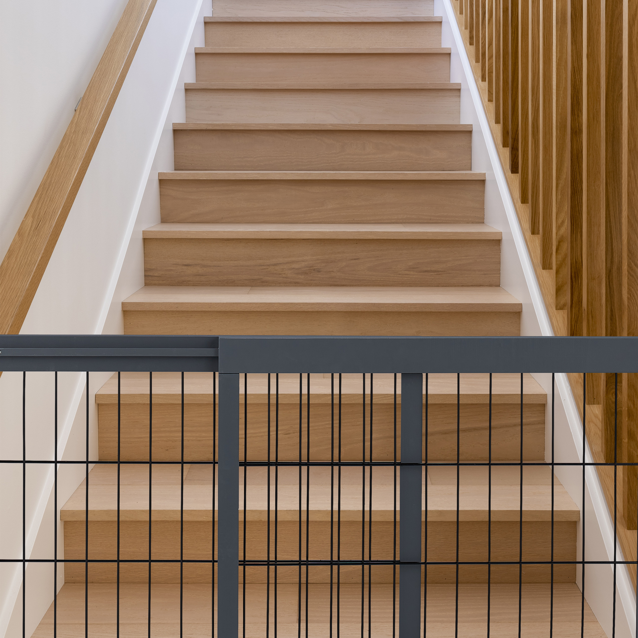 Eine gerade Holztreppe mit passendem Geländer und einem grauen Schutzgitter unten.