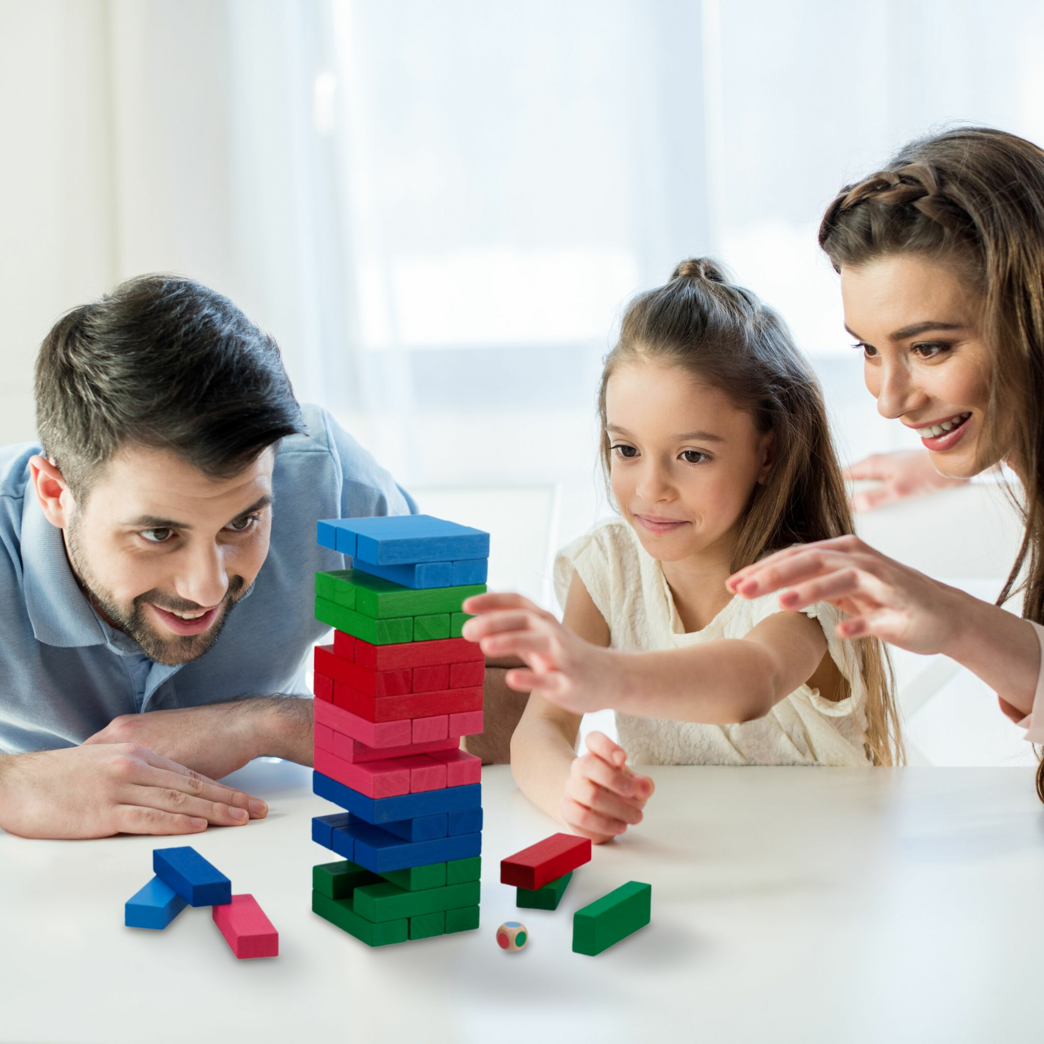 Eine Familie spielt zusammen Jenga an einem weißen Tisch.