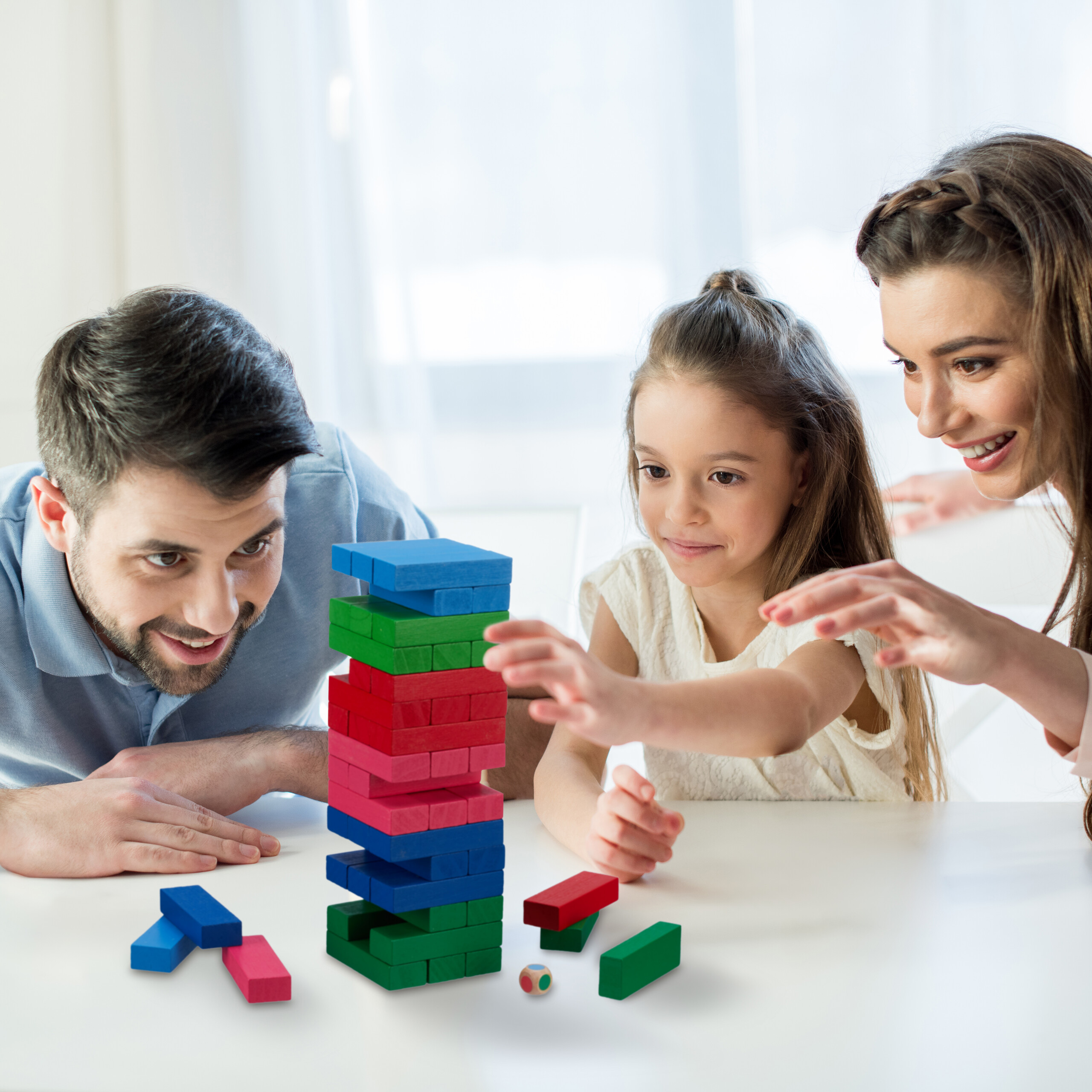 Eine Familie spielt zusammen ein buntes Holzklötzchenspiel am Tisch.