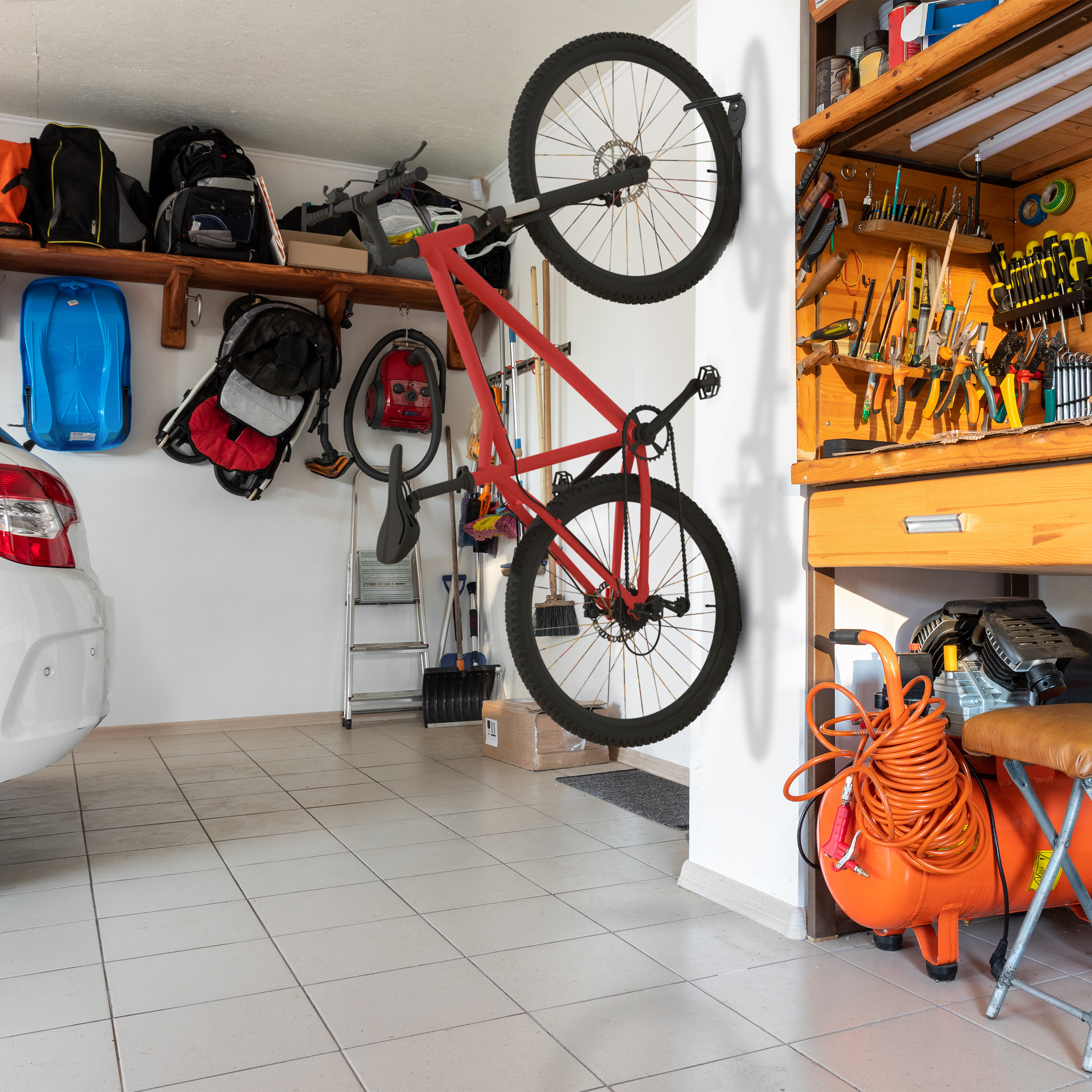 Eine rote Fahrrad hängt an der Wand in einer Garage neben einem Werkzeugregal und einem Auto.