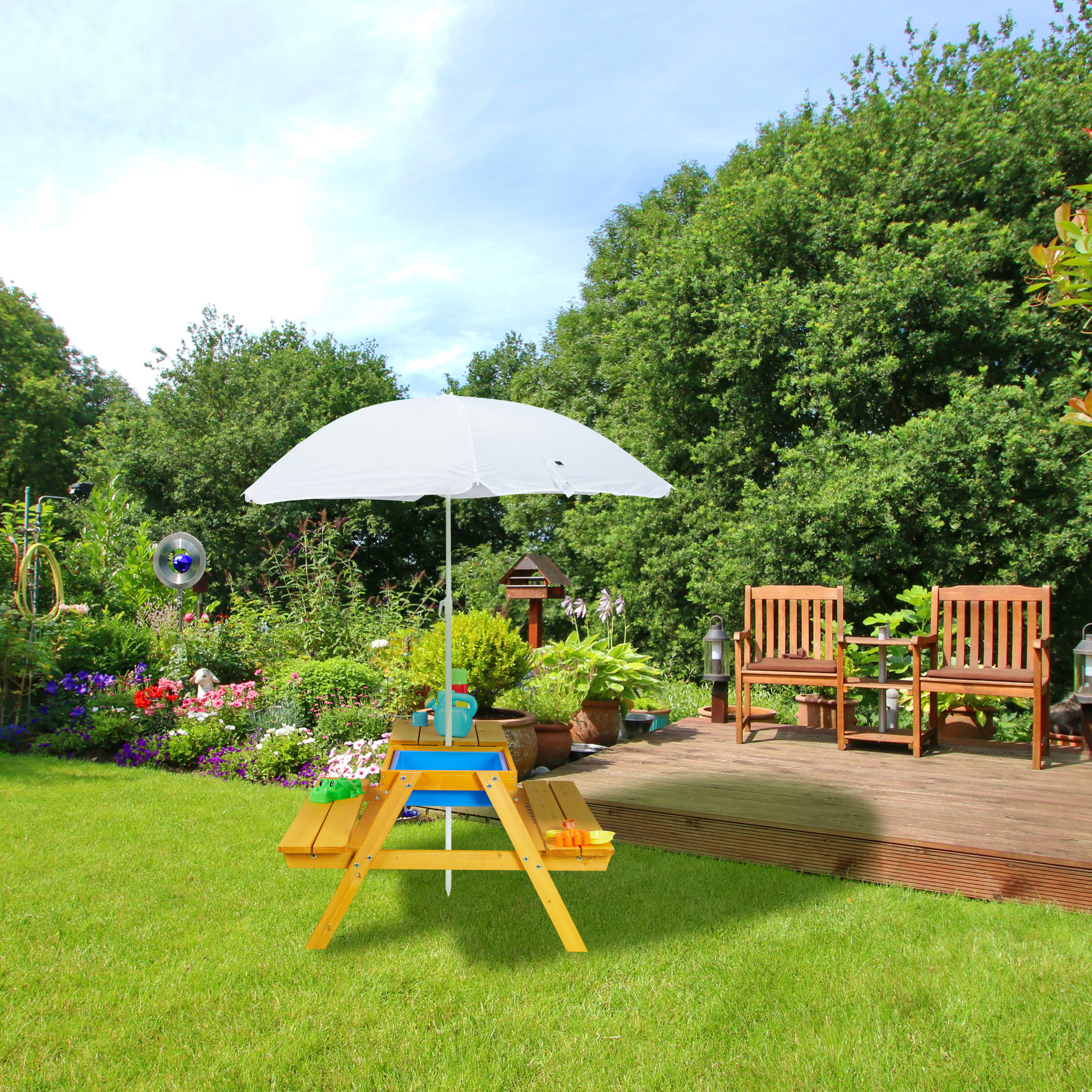 Ein kleiner Holztisch mit weißem Sonnenschirm auf grünem Rasen vor einem Garten und Holzdeck.