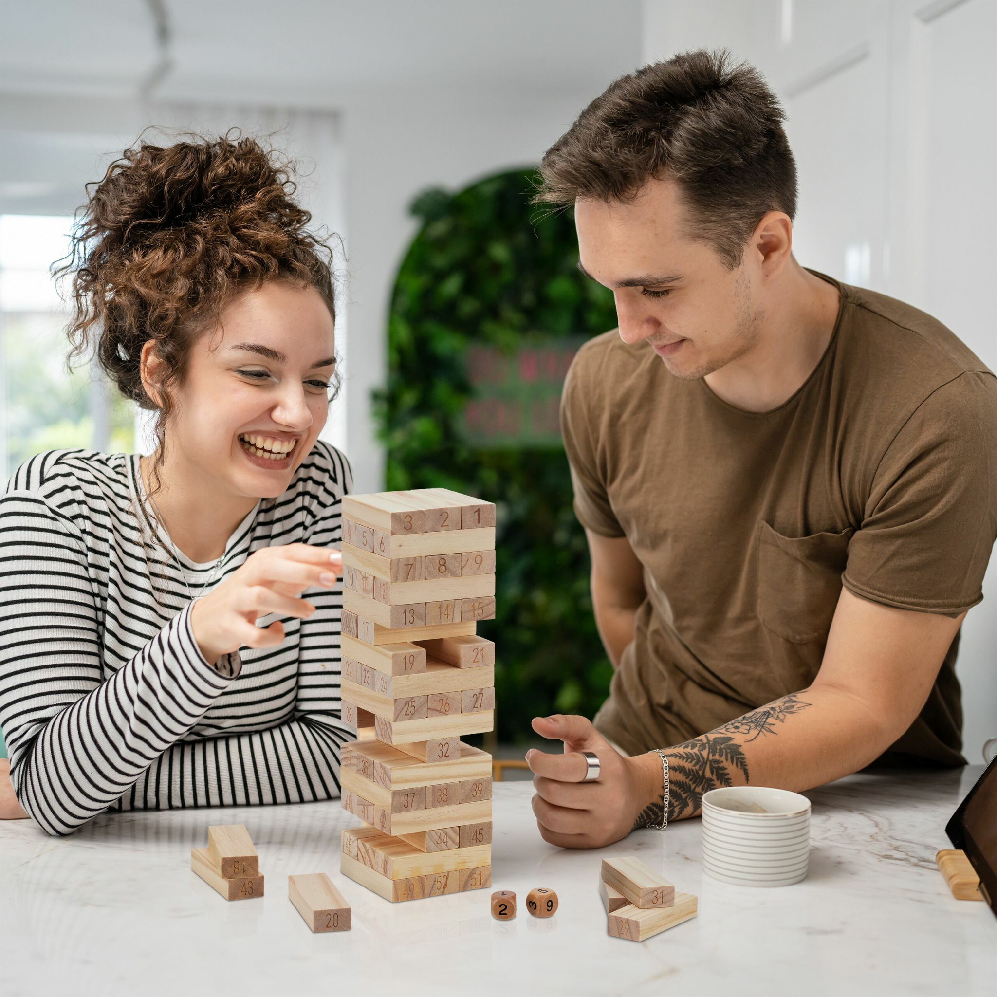 Ein junges Paar spielt zu Hause ein Holzturm-Spiel und lächelt.
