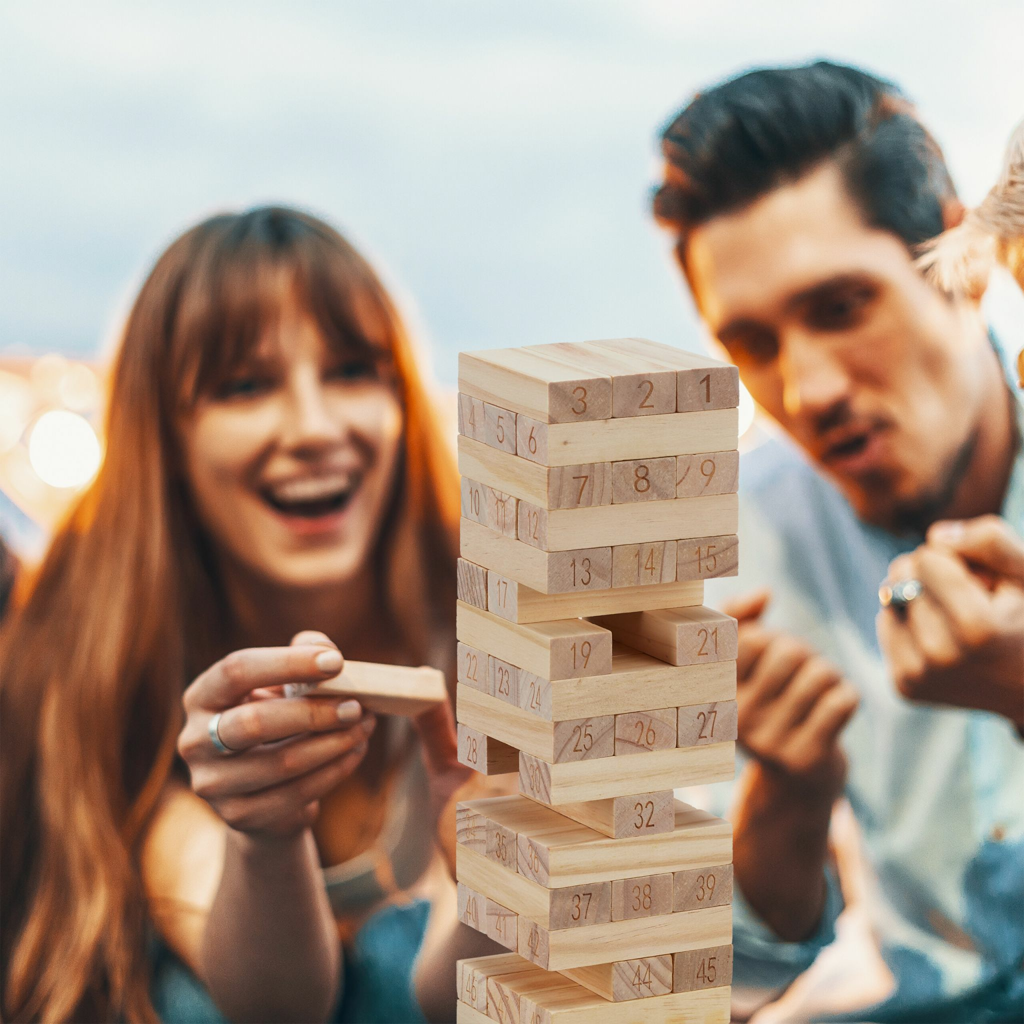 Eine junge Frau und ein Mann lachen, während sie ein Turmbau-Spiel aus Holz spielen.